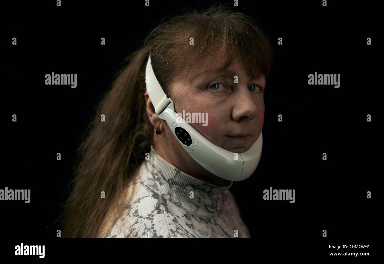 Portrait d'une femme adulte mature avec dispositif de levage du visage et de photonthérapie sur fond noir Banque D'Images