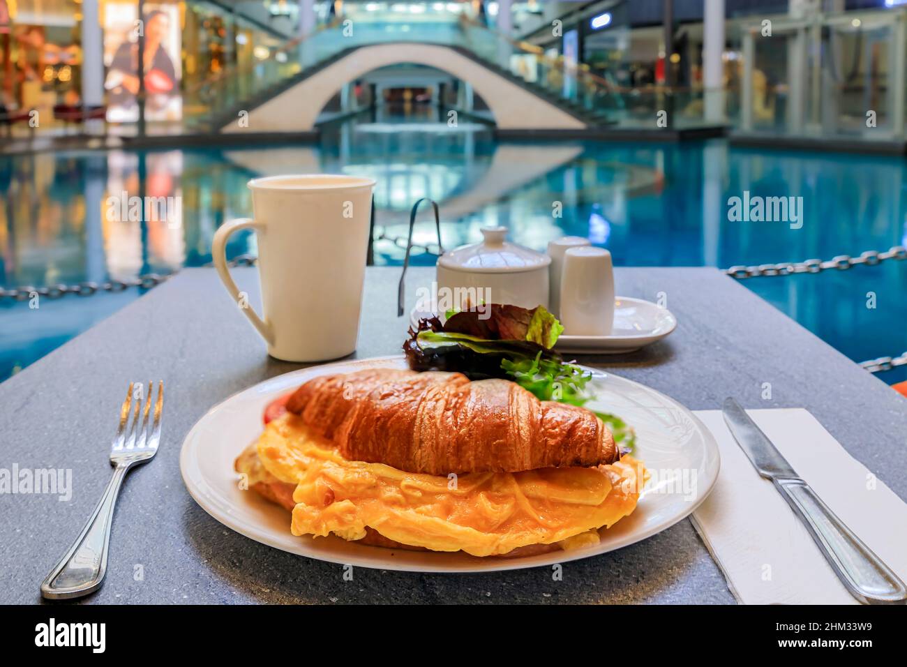 Une tasse de café avec un croissant et un sandwich aux œufs au petit-déjeuner dans un café situé dans un centre commercial de luxe avec des restaurants et des boutiques haut de gamme, à Singapour Banque D'Images