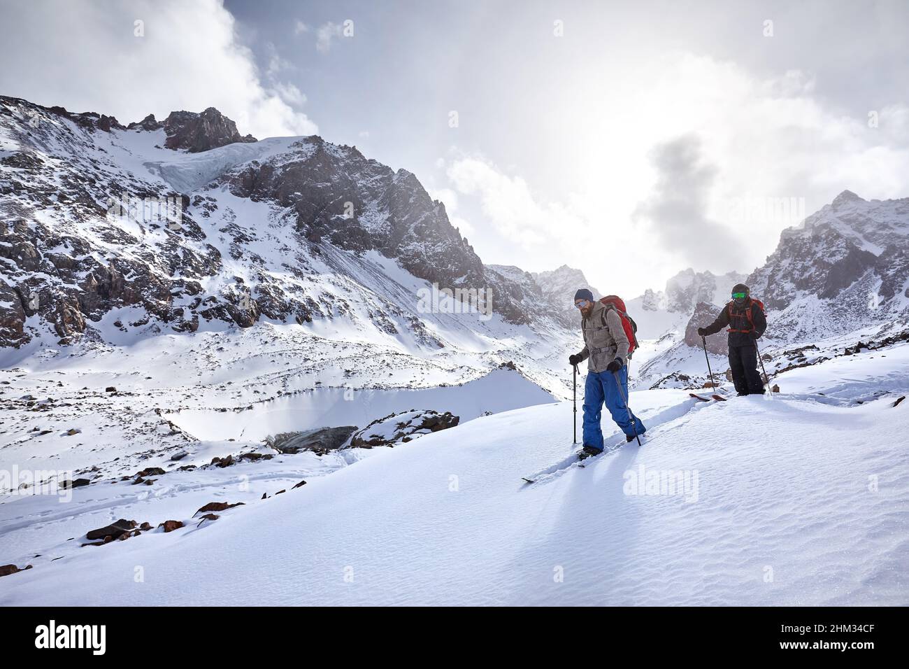 Deux skiers ski alpin avec une barbe et un sac à dos dans un casque et un masque dans des montagnes enneigées. Sport en plein air dans l'arrière-pays en hiver. Banque D'Images