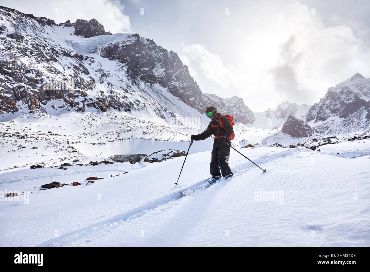 Skieur ski alpin avec sac à dos rouge dans un casque et un masque dans des montagnes enneigées. Sport en plein air en hiver Banque D'Images