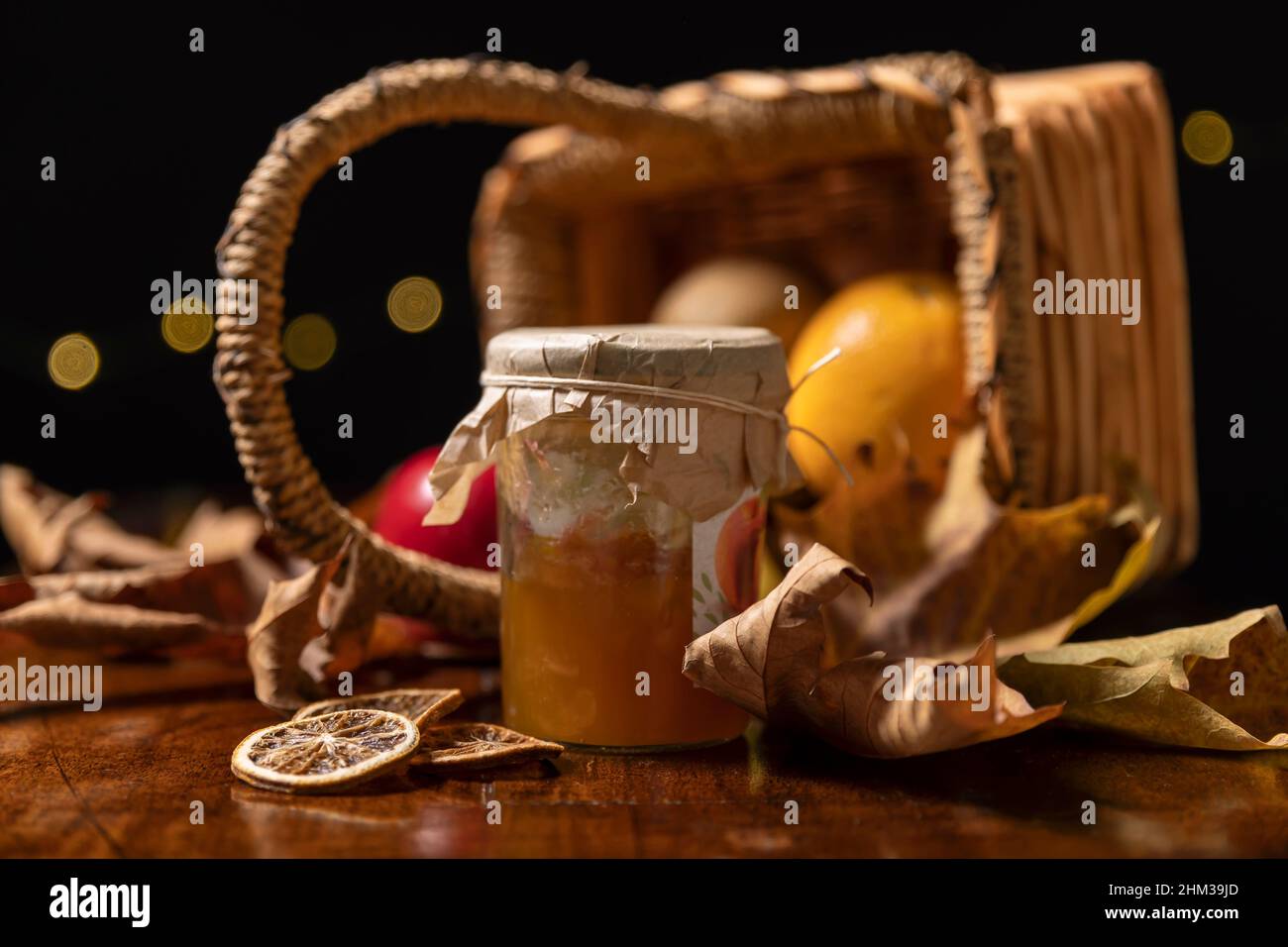 Un pot de confiture de pêche avec des tranches d'orange séchées avec un panier en osier renversé et des feuilles sèches en arrière-plan Banque D'Images