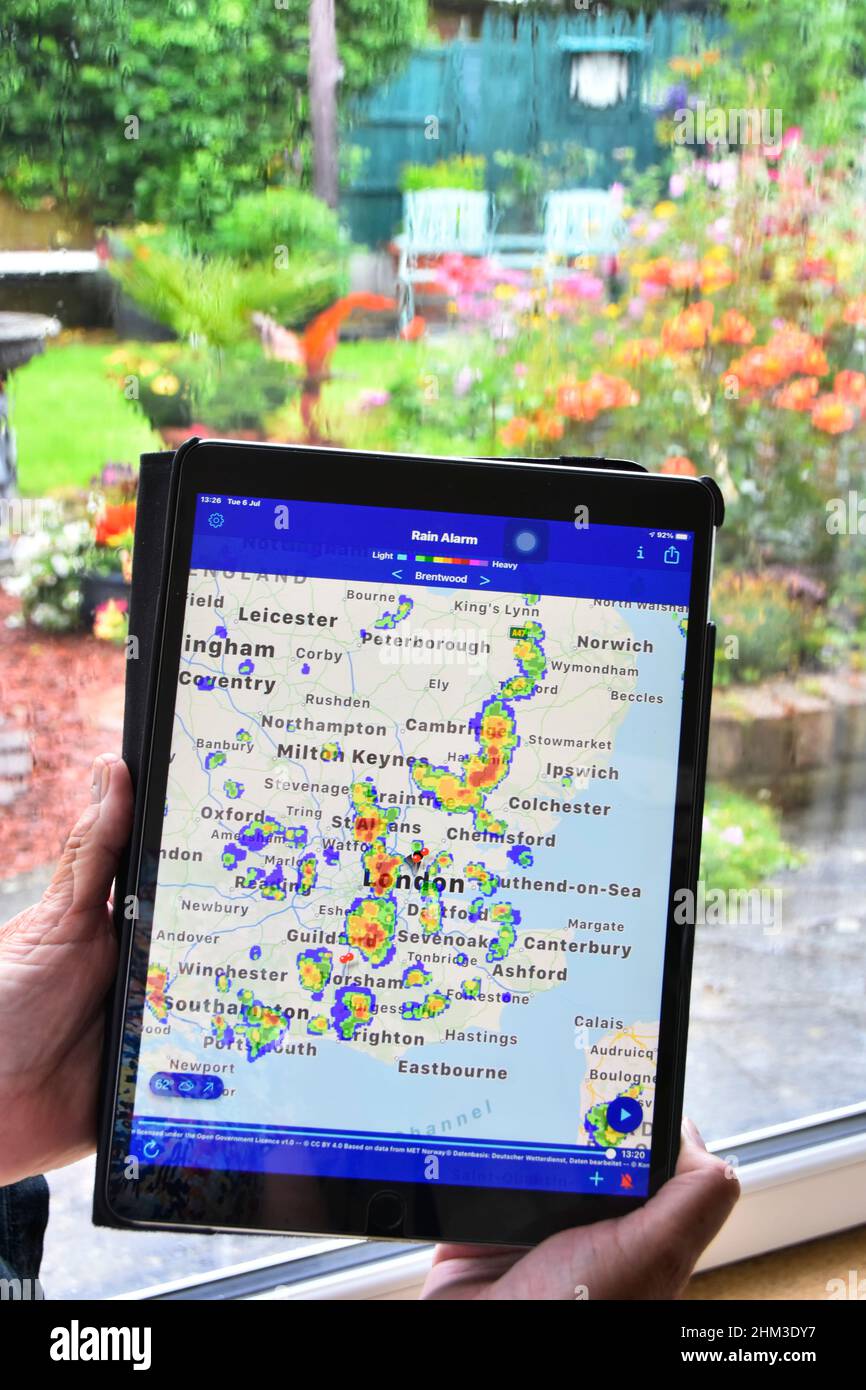 Les données de l'application de radar en couleur en temps réel pour ipad montrent les précipitations sur la carte locale, la femme attend que le temps humide s'efface sur la fenêtre de la maison revenir à jardinage Essex Royaume-Uni Banque D'Images