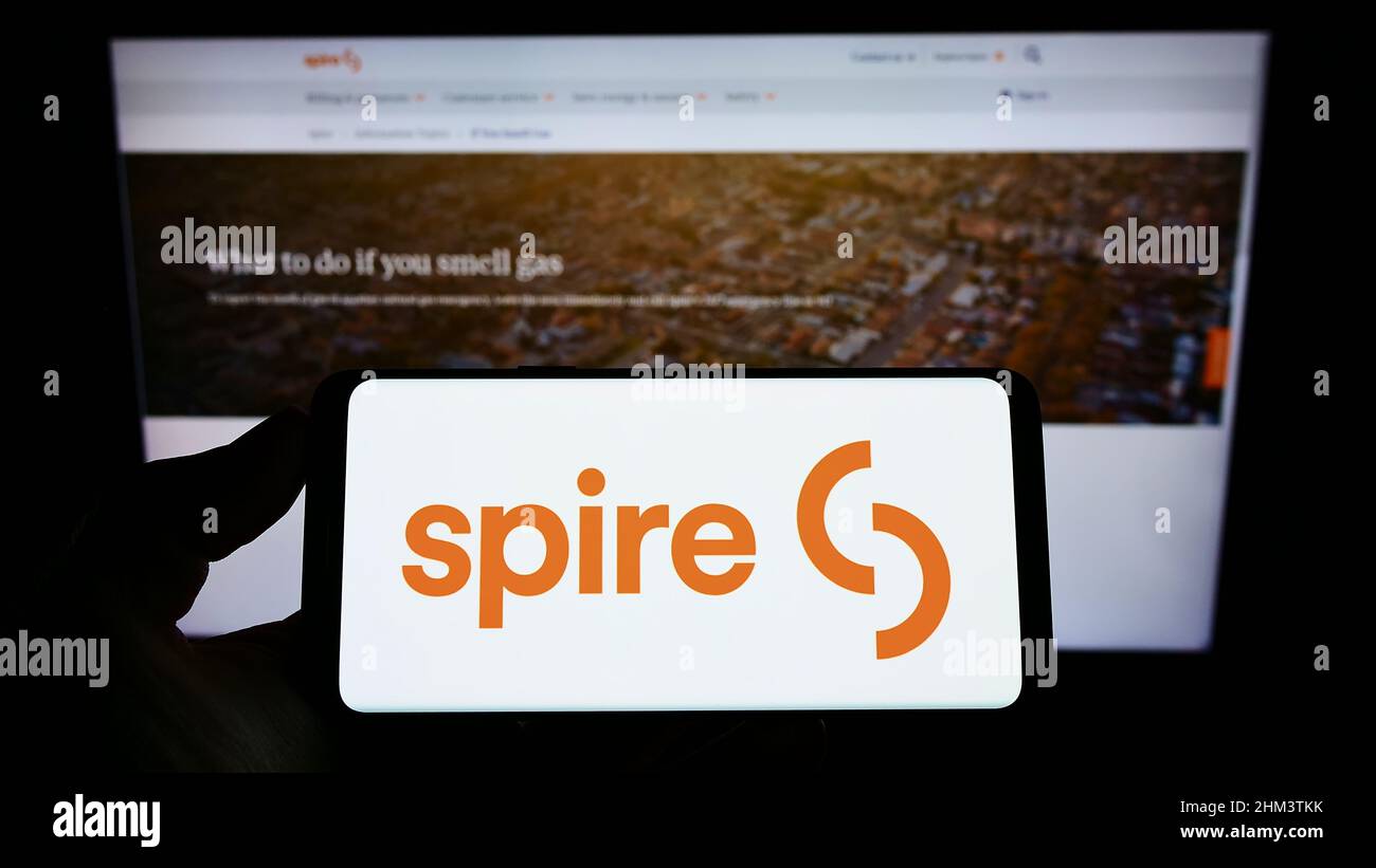 Personne tenant un téléphone portable avec le logo de la société de services publics américaine Spire Inc. À l'écran en face de la page Web d'affaires. Mise au point sur l'affichage du téléphone. Banque D'Images