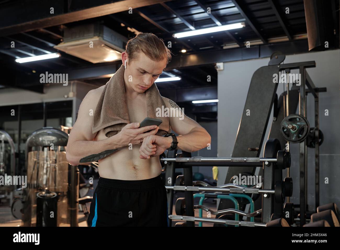 Athlète musclé sérieux vérifiant les résultats sportifs sur l'application smartphone et la montre intelligente après une bonne séance d'entraînement dans la salle de fitness Banque D'Images