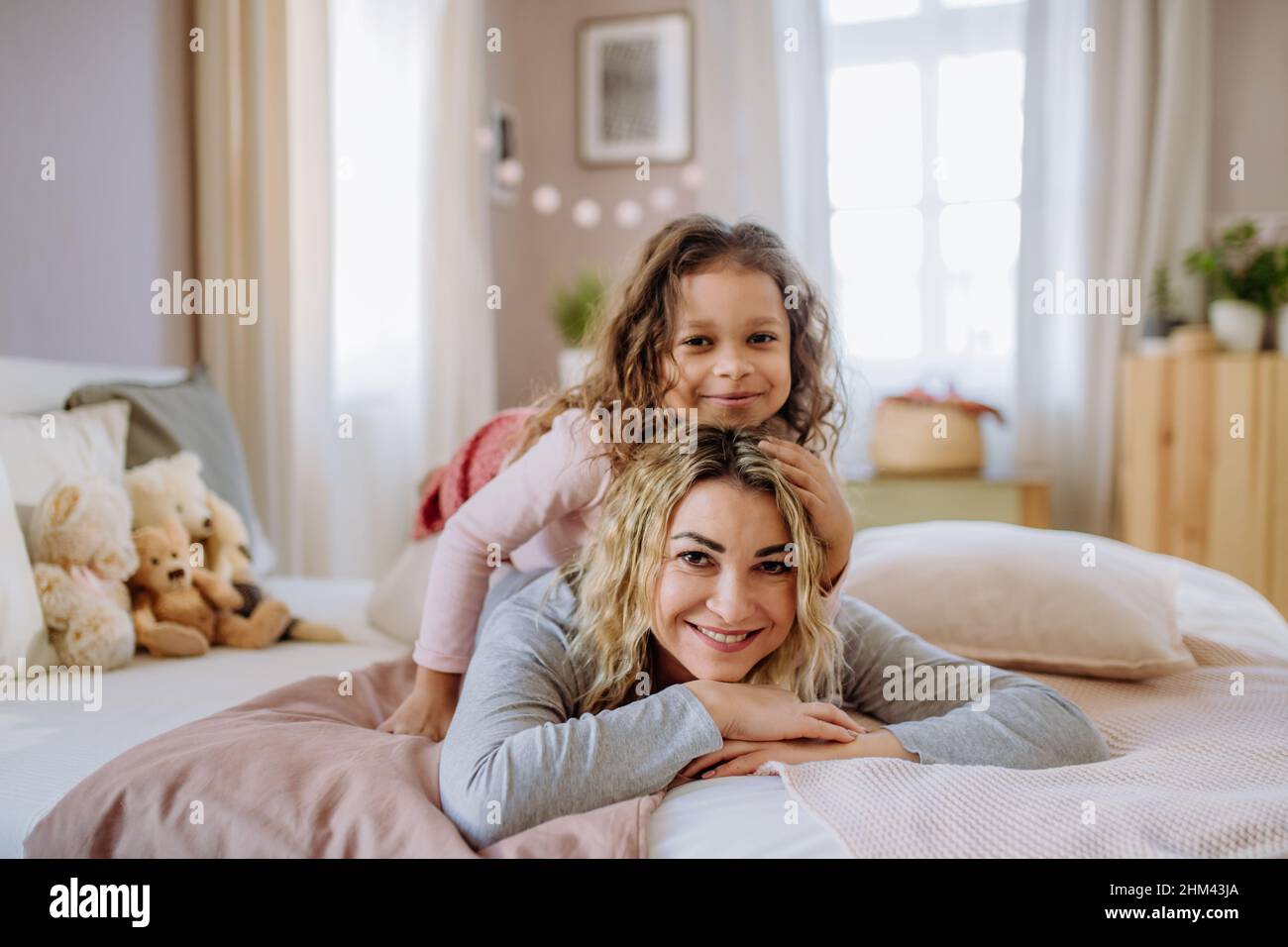 Bonne petite fille allongé sur les mères dos sur le lit et regardant l'appareil photo à la maison. Banque D'Images