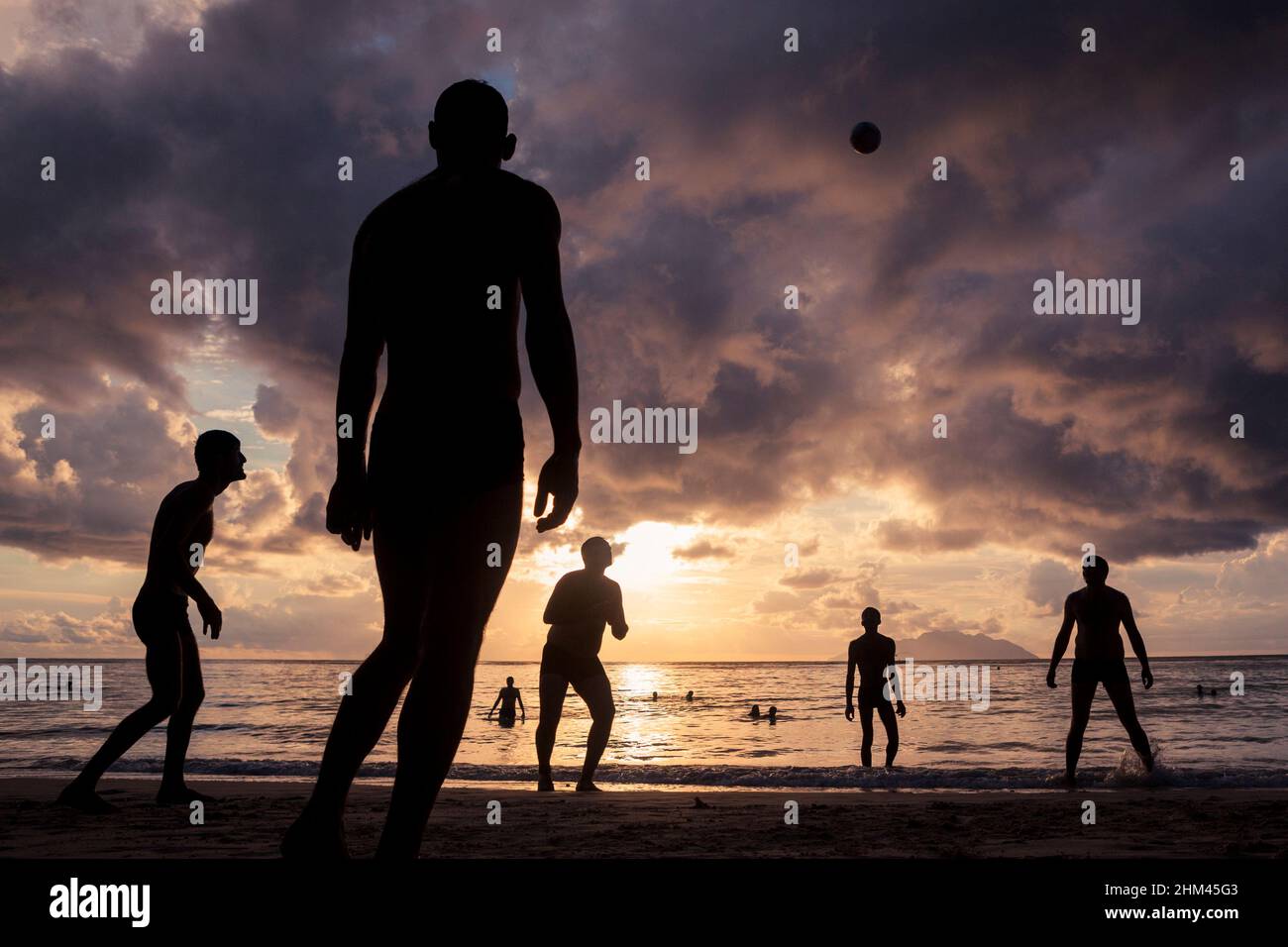Silhouettes sur la plage de beau Vallon jouant au volley-ball au coucher du soleil sur l'île de Mahé, Seychelles. Banque D'Images