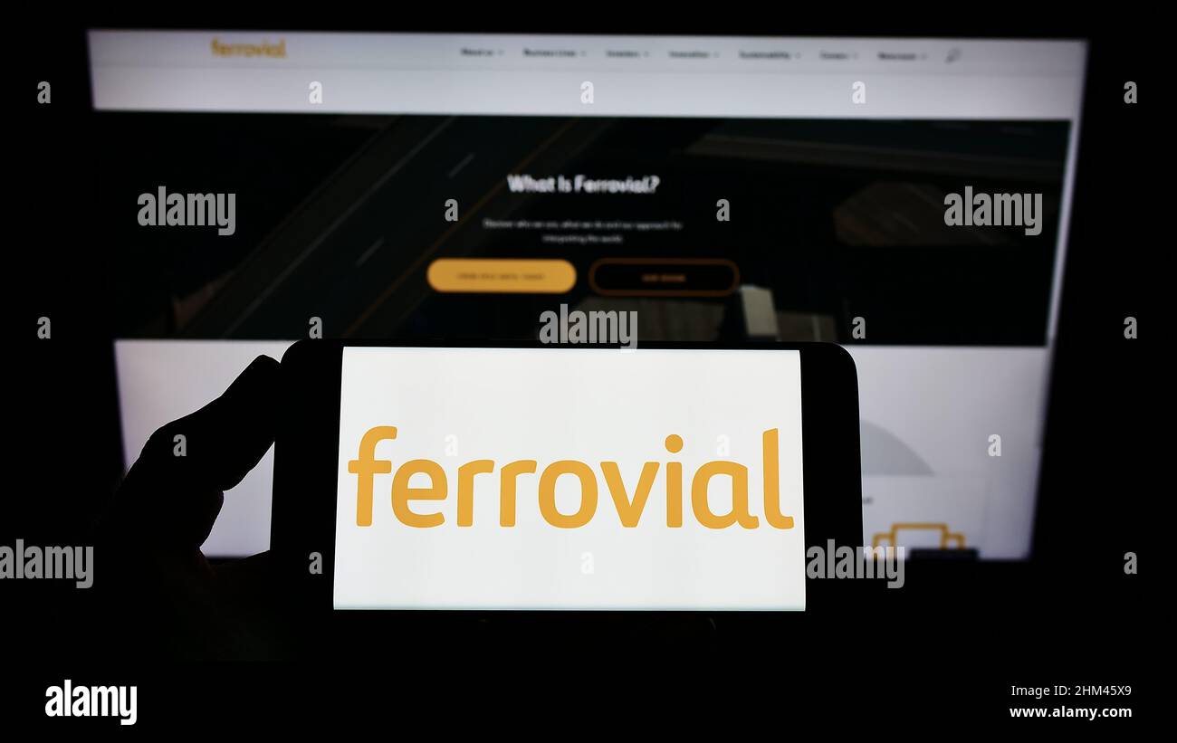 Personne tenant un smartphone avec le logo de la société de construction espagnole Ferrovial S.A. sur écran devant le site. Mise au point sur l'affichage du téléphone. Banque D'Images