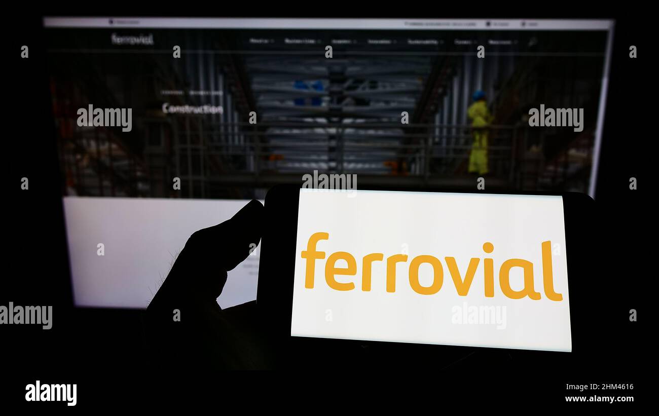 Personne tenant un téléphone portable avec le logo de la société espagnole de construction Ferrovial sa à l'écran en face de la page web d'affaires. Mise au point sur l'affichage du téléphone. Banque D'Images