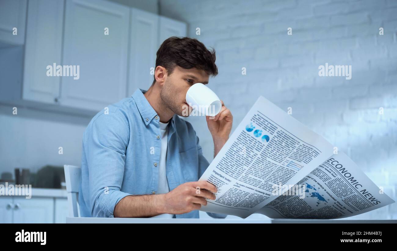 homme en chemise bleue, qui boit du café et lit le journal du matin dans la cuisine Banque D'Images