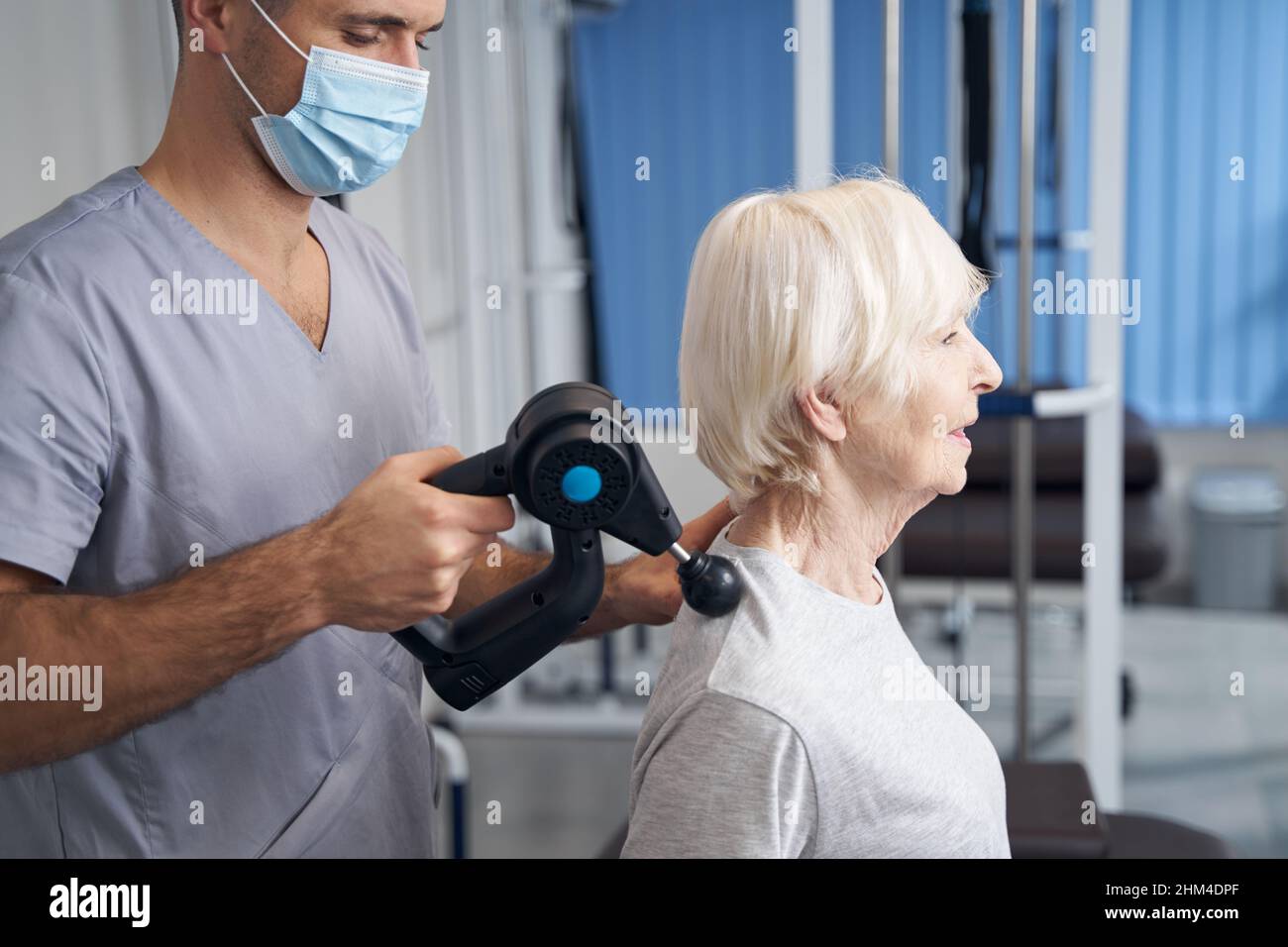 Physiothérapeute traitant l'épaule du retraité avec un pistolet de massage musculaire Banque D'Images