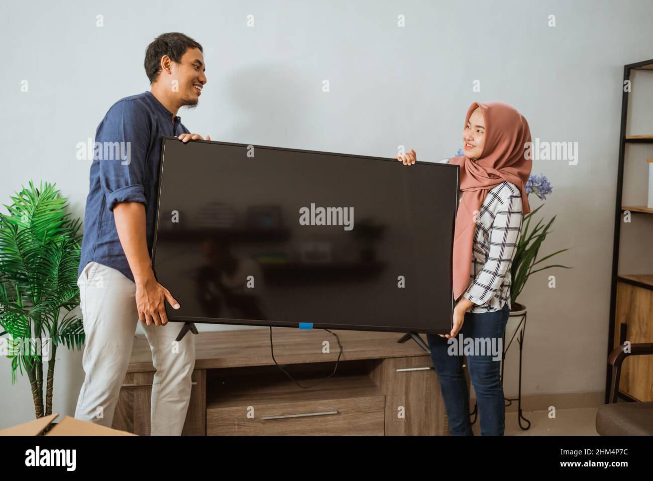 Couple musulman portant un écran plat dans leur maison moderne Banque D'Images