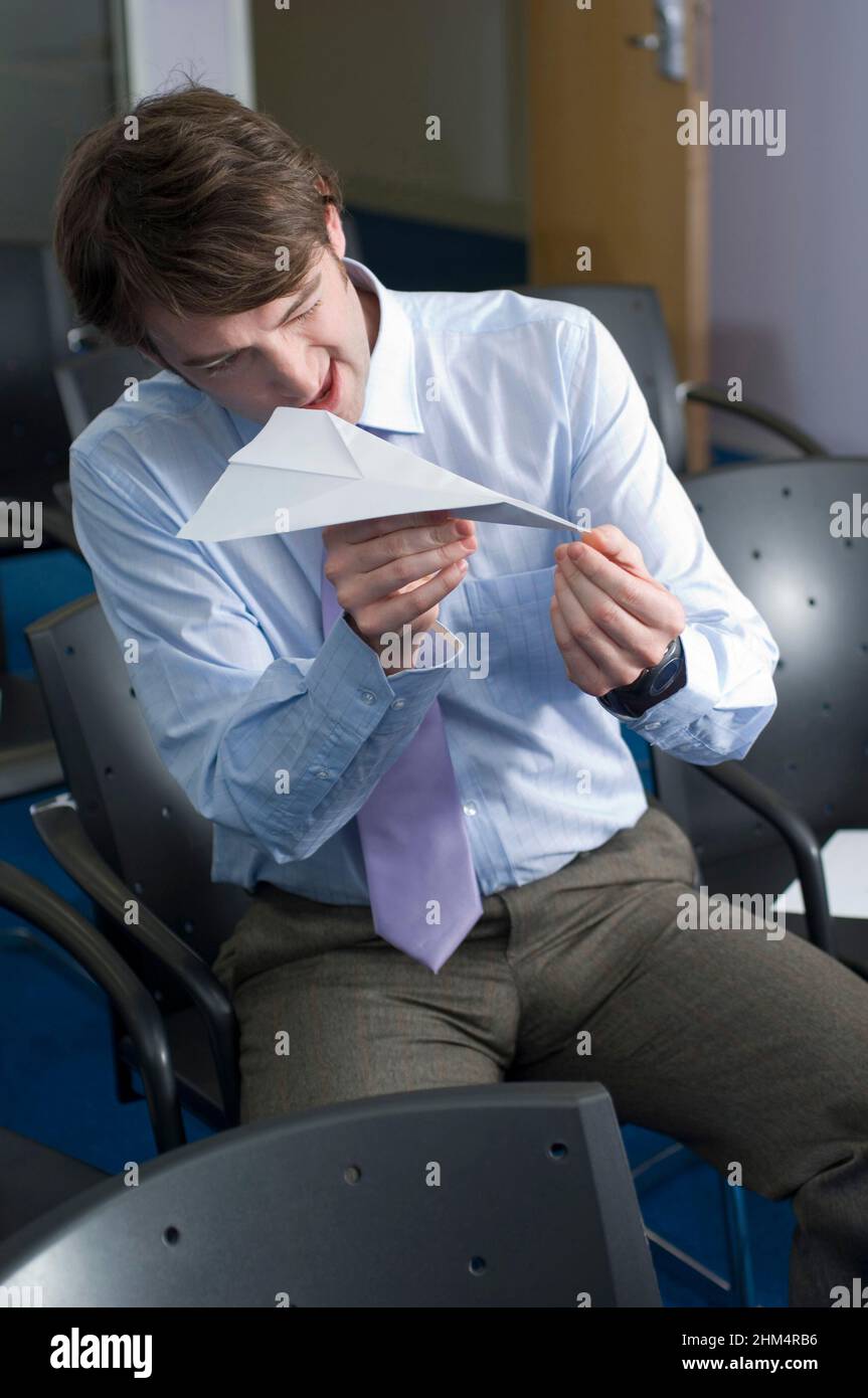 Homme d'affaires assis sur une chaise et tenant Un avion papier, crédit:Photoshhot Creative / Stuart Cox / Avalon Banque D'Images