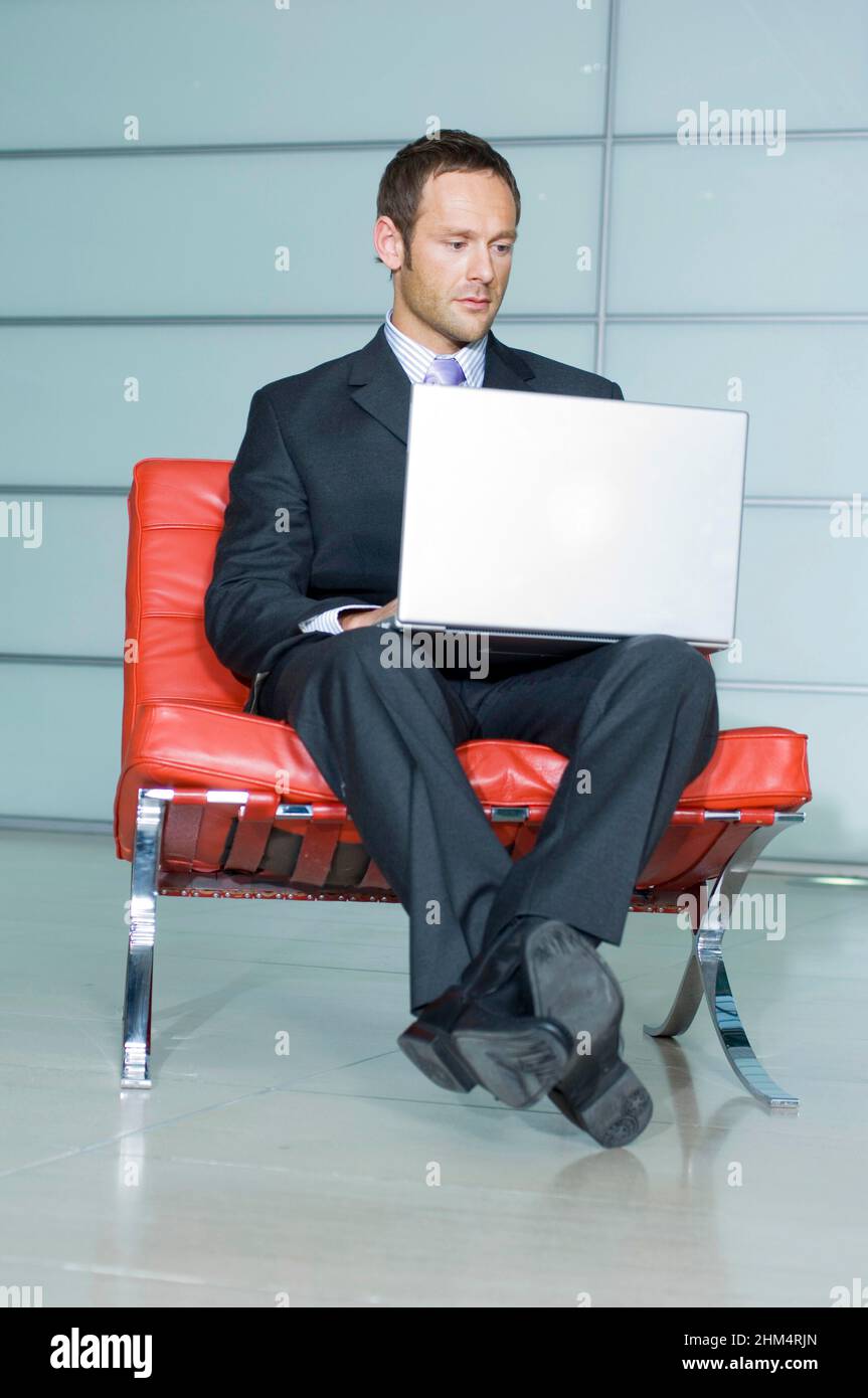 Homme d'affaires assis sur une chaise et à l'aide D'un ordinateur portable, Credit:Photoshhot Creative / Stuart Cox / Avalon Banque D'Images