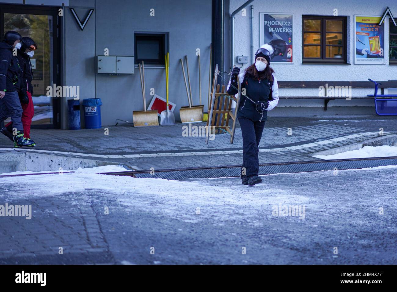 Une femme portant un masque Corona porte son traîneau et traverse la voie ferrée à la gare d'Eibsee à Zugspitze. Banque D'Images