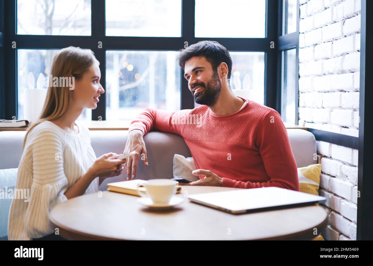 Couple positif communiquant tout en étant assis dans un café confortable avec des smartphones Banque D'Images