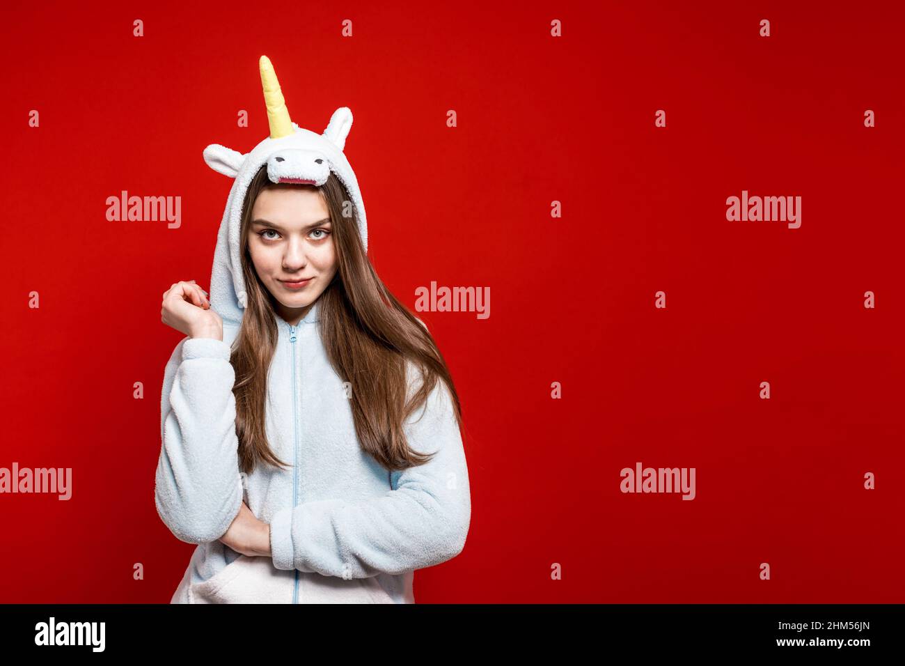 Fête de poules. Fête de pyjama. Une fille avec un pyjama unicorn sur fond rouge regarde sur le côté. Banque D'Images