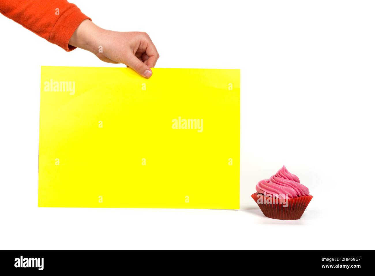 Main tenant le papier jaune vierge pour petit cupcake rose isolé sur un blanc. Banque D'Images
