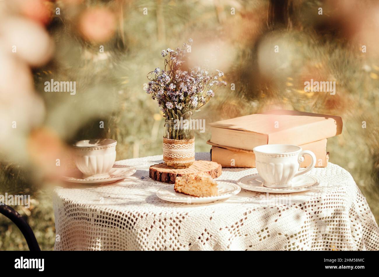 Rêvez d'une vue à travers les fleurs de pomme jusqu'à la table, avec des tasses à thé et des livres. Bouquet de fleurs sauvages Myosotis arvensis Forget me nots in fait main pot. Banque D'Images