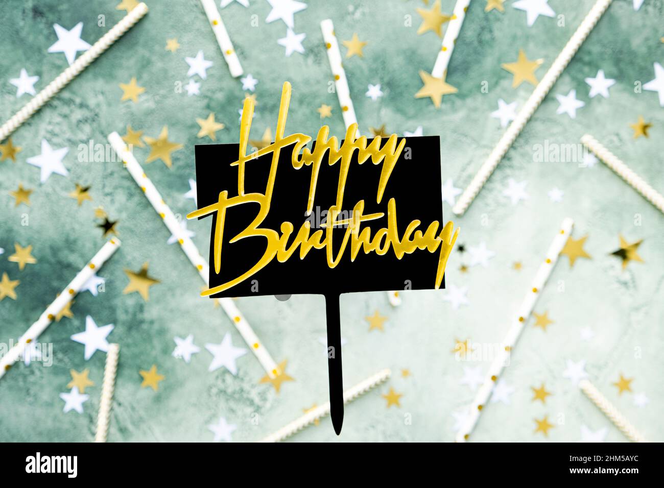 Lettrage doré joyeux anniversaire sur plaque noire avec stylo sur fond vert flou avec étoiles et pailles pour cocktail. Carte d'anniversaire de fête Banque D'Images