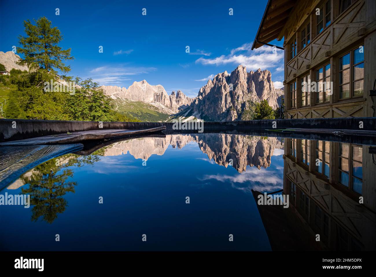 Les principaux sommets du groupe Rosengarten se reflètent dans un bain rempli d'eau, une maison en bois à côté. Banque D'Images