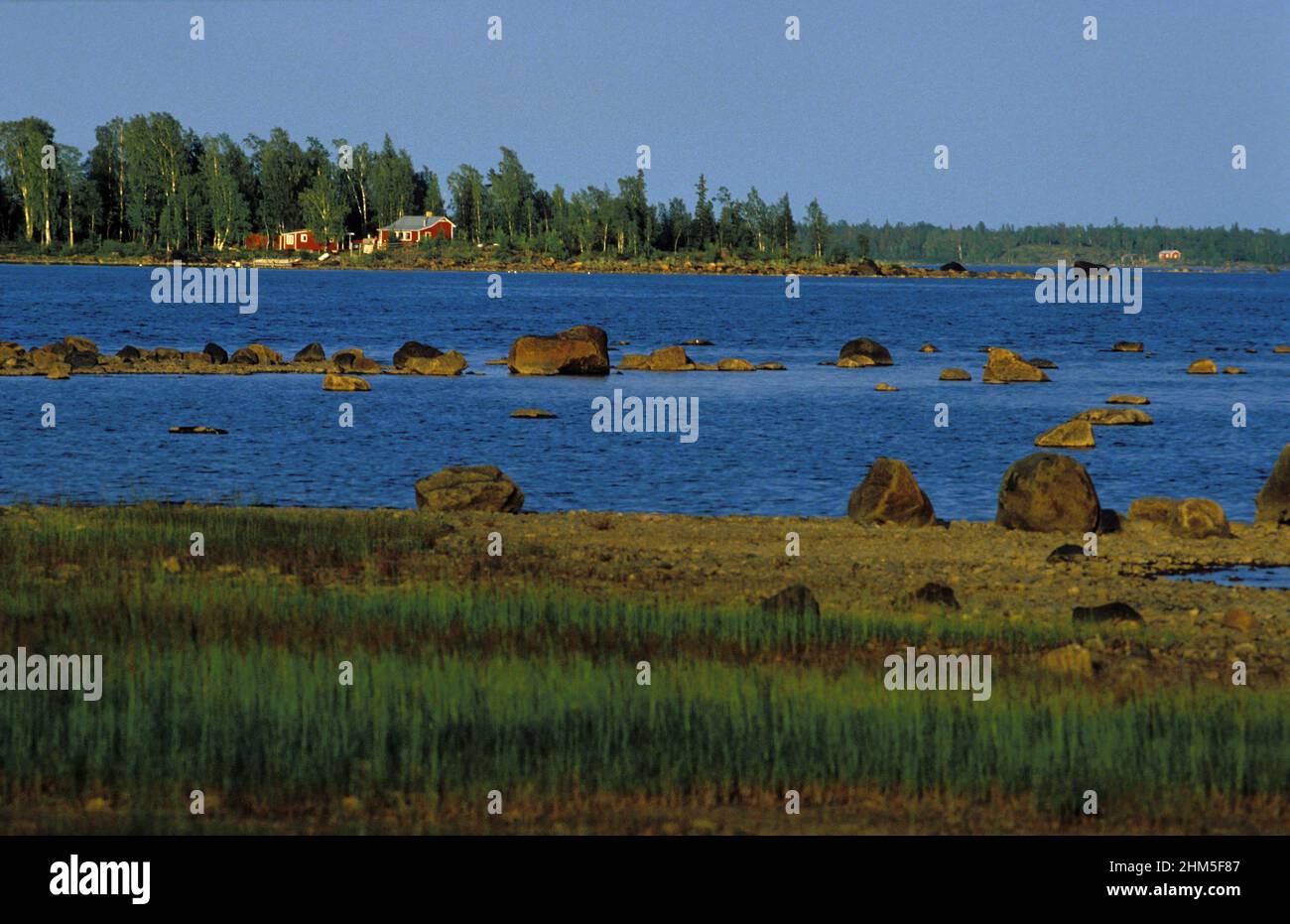 Rivage et rivage de la mer Baltique en 1989, analogique. Petites cabanes rouges sur une île, eau, et roseau de ce côté. Banque D'Images
