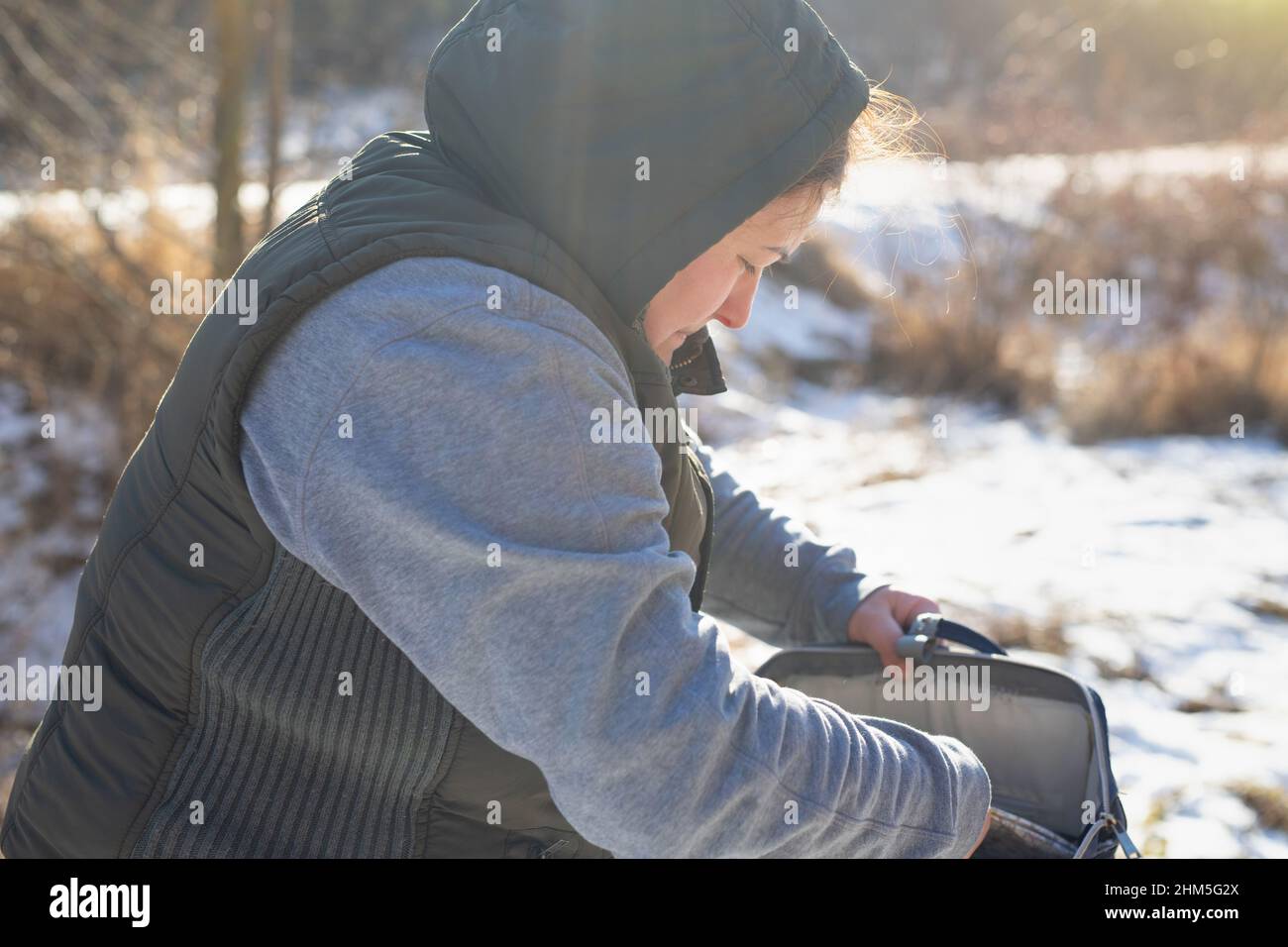 Vue latérale photo d'une femme voyageur dans des vêtements chauds dehors le jour ensoleillé de neige ouvrir son sac et à la recherche de quelque chose. Banque D'Images