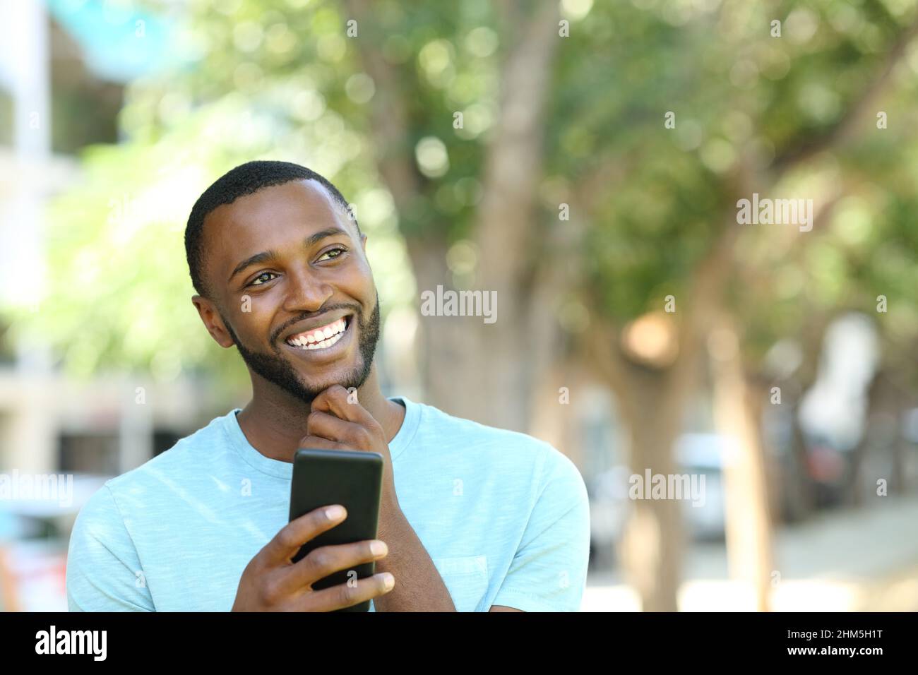 Homme heureux avec la peau noire pensant tenir le smartphone dans un parc Banque D'Images