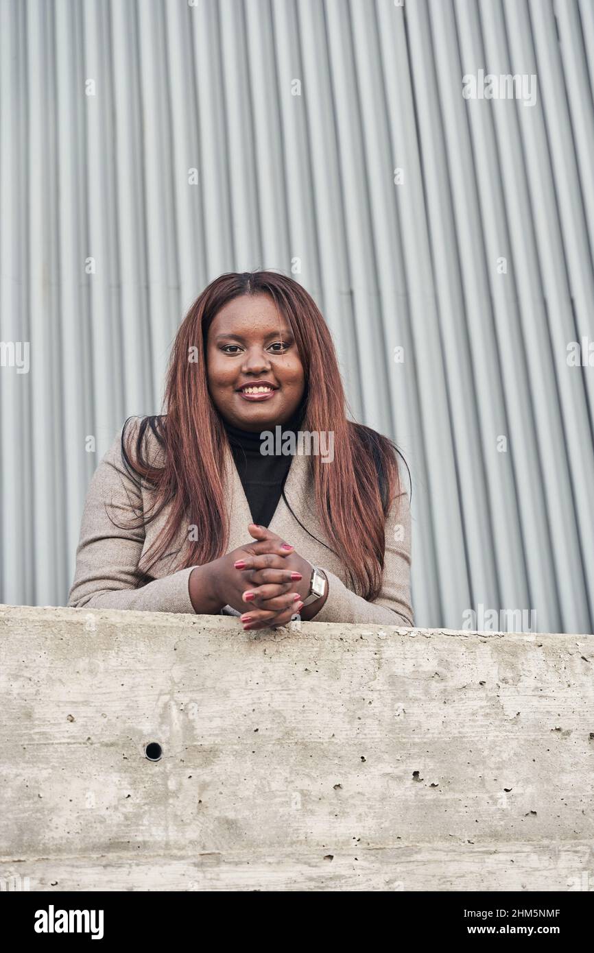 portrait de la jeune femme afro-américaine en costume avec de longs cheveux regardant l'appareil photo avec ses mains sur un mur. Banque D'Images