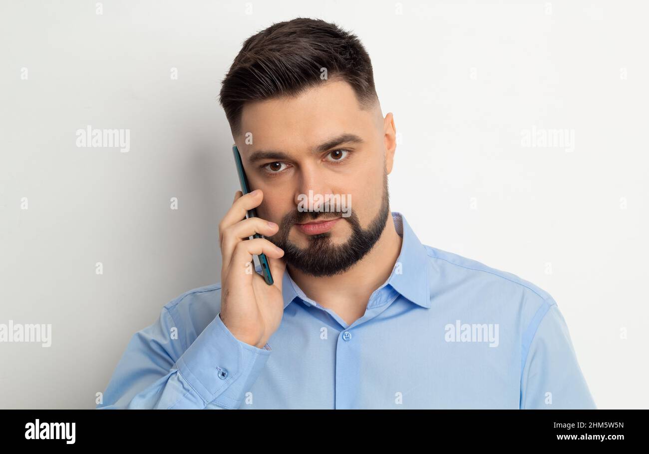 Portrait d'un homme d'affaires avec une barbe parlant sur un téléphone portable sur un fond blanc. Banque D'Images