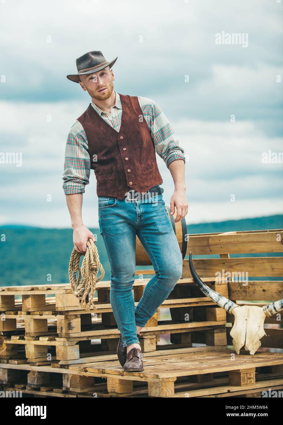 Cow-boy américain. Charmant gars brutal de l'Ouest. Cowboy avec corde de lasso sur fond de ciel. Banque D'Images