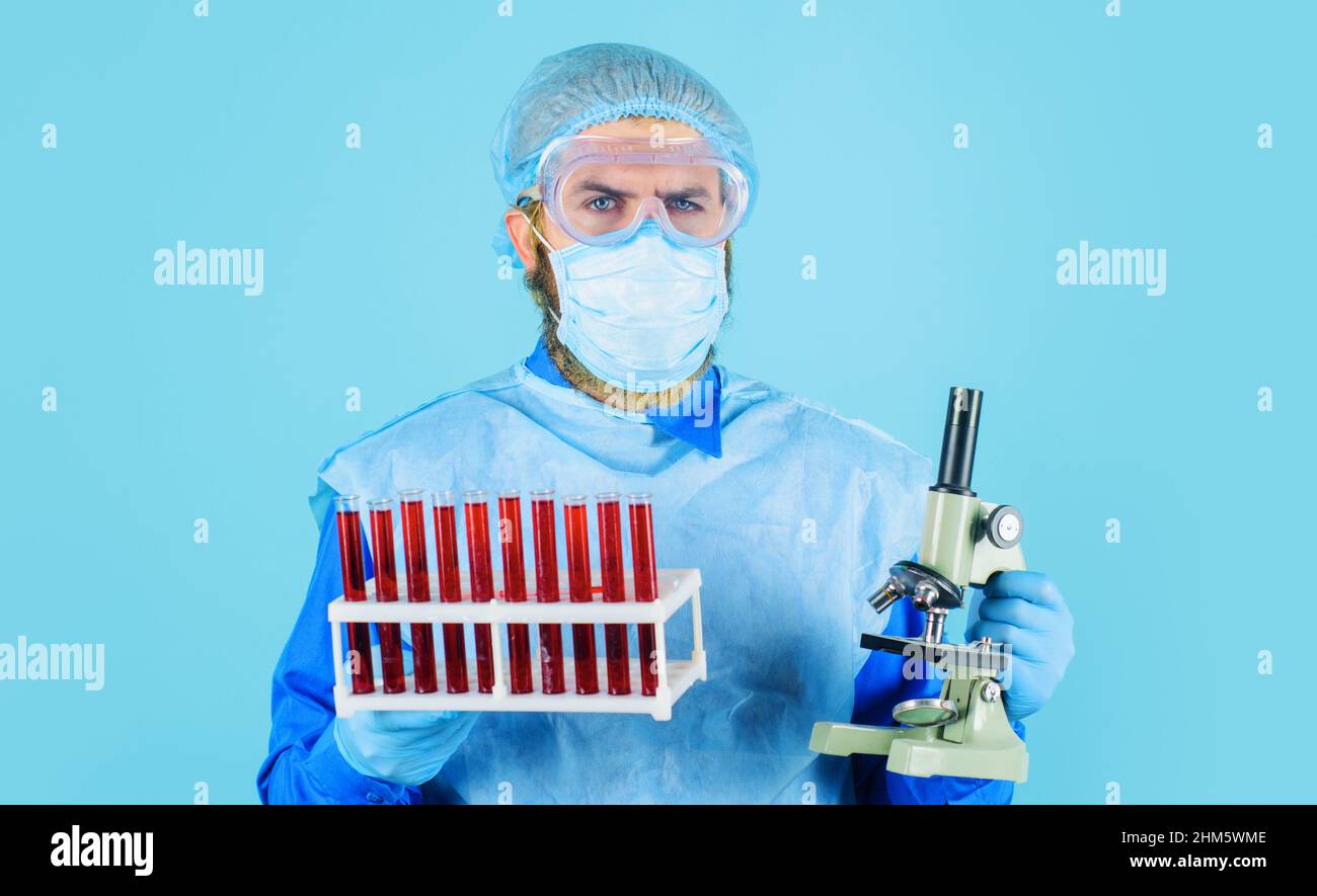 Médecin en masque médical avec tubes à essai et microscope. Un scientifique analysant un échantillon de sang en clinique. Banque D'Images