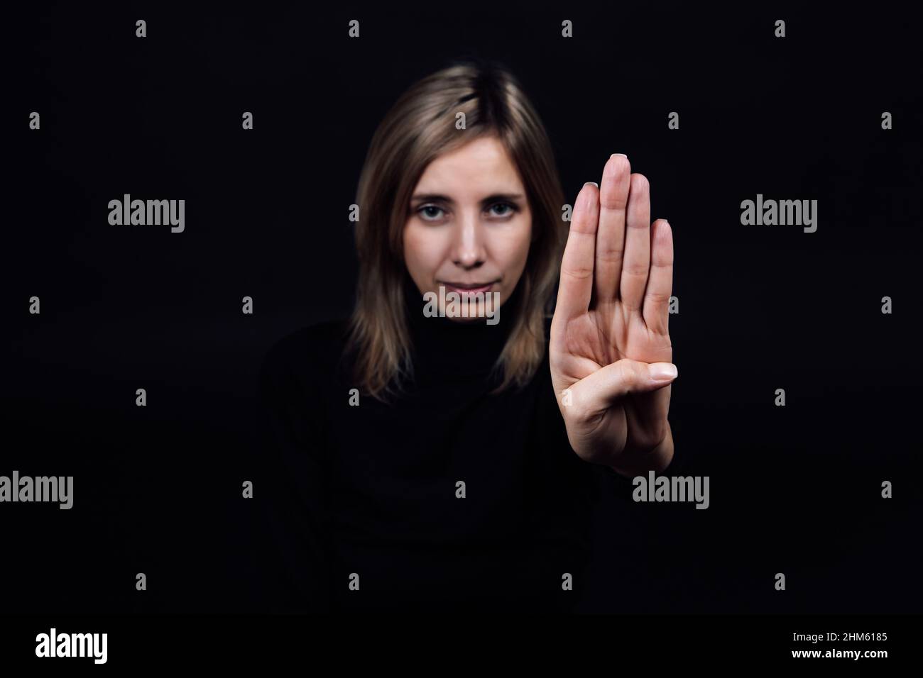 Une jeune femme demande de l'aide pour les agressions et les abus domestiques en montrant un panneau d'arrêt avec la main regardant la caméra sur fond noir. Agression relative Banque D'Images