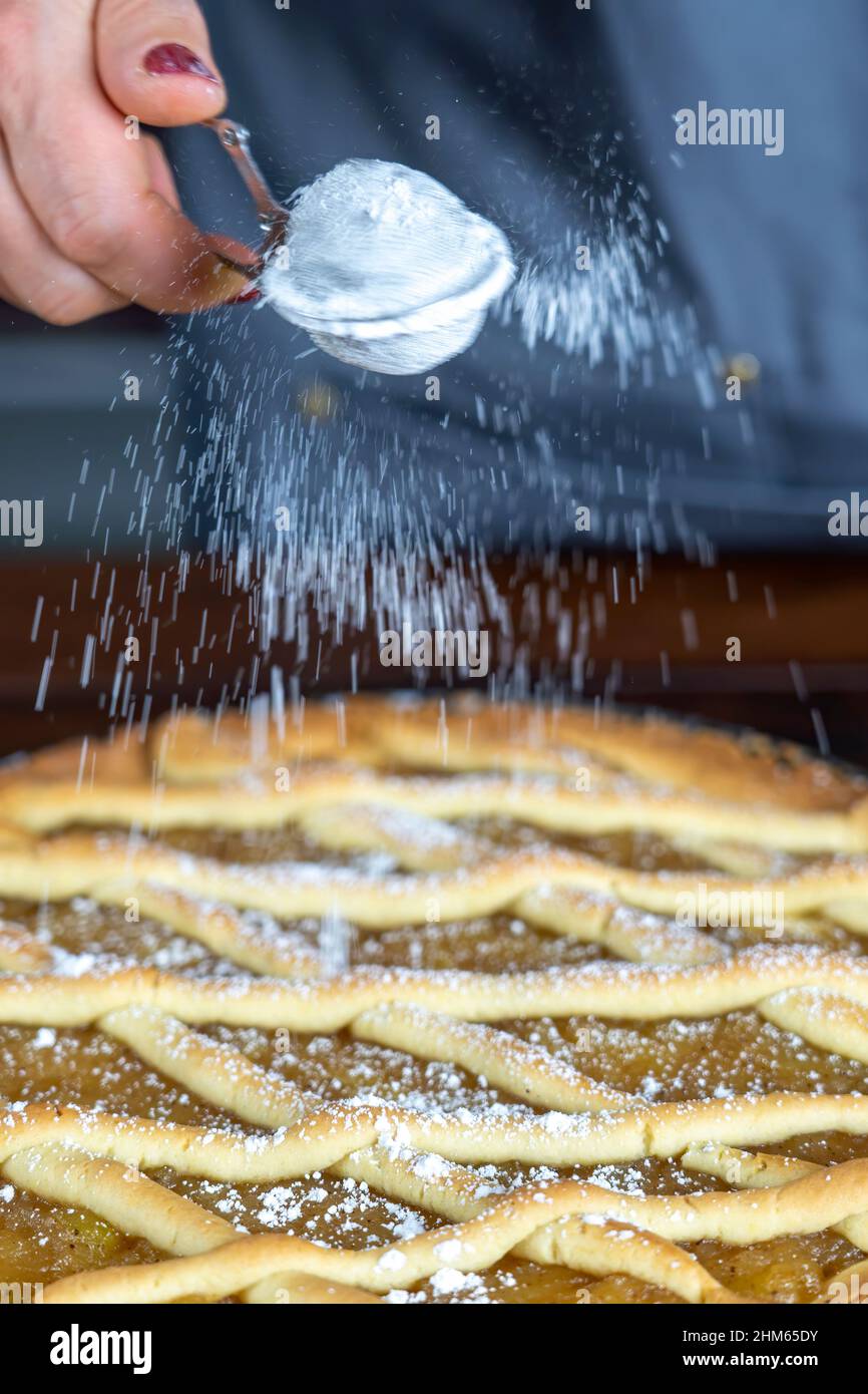 Les femmes préparant une tarte aux pommes ou une grande tarte sur fond de table en bois. Saupoudrer de sucre en poudre. Banque D'Images