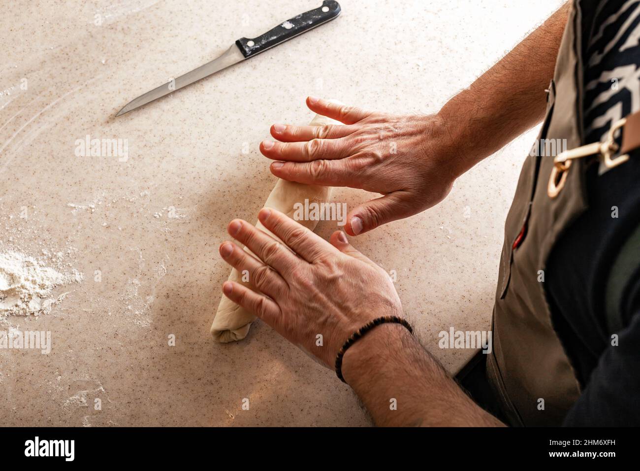 Les mains de sexe masculin pétrir la pâte. Mains humaines préparant la pâte pour la baguette maison. Banque D'Images