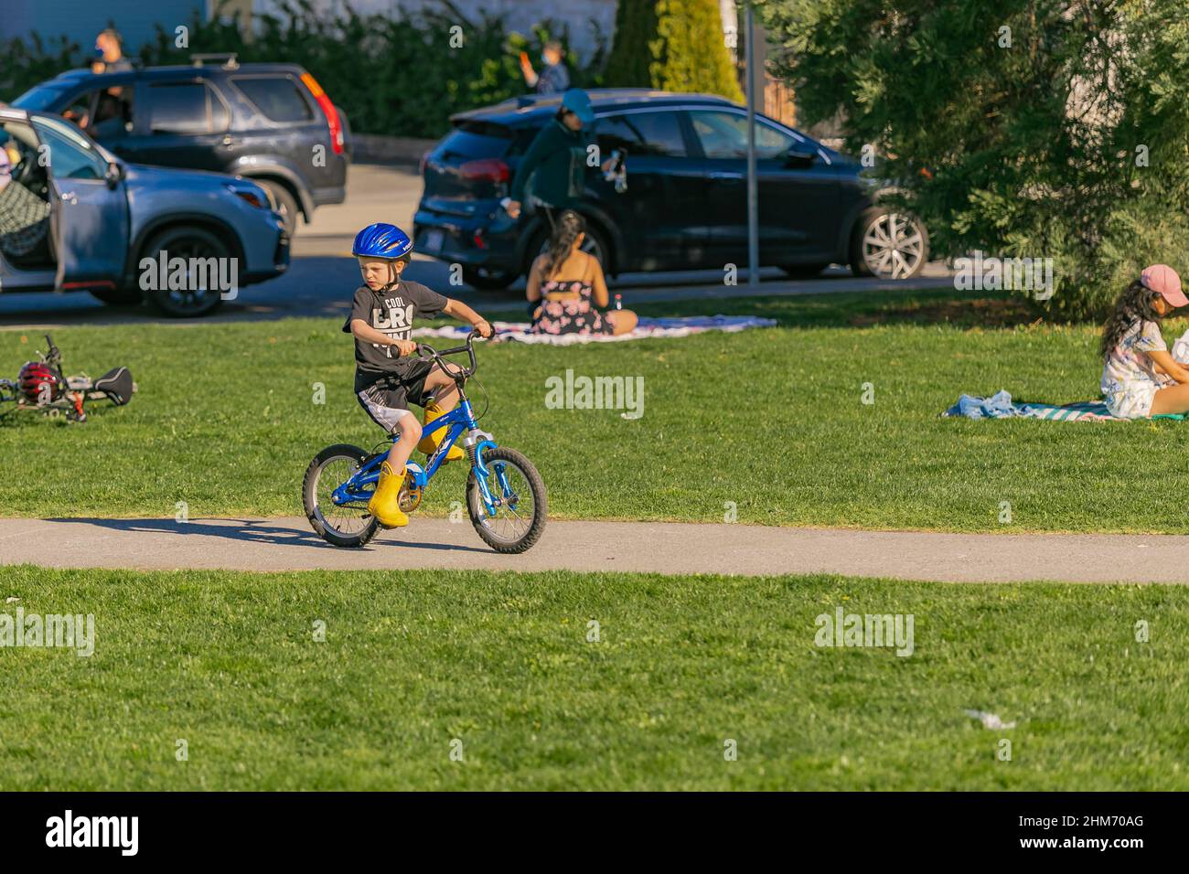 Un garçon avec un casque de vélo vert sur sa tête roule son vélo dans le parc d'été. Repos d'été. Garçon apprenant à faire son vélo-avril 18,2021-Richmond Banque D'Images