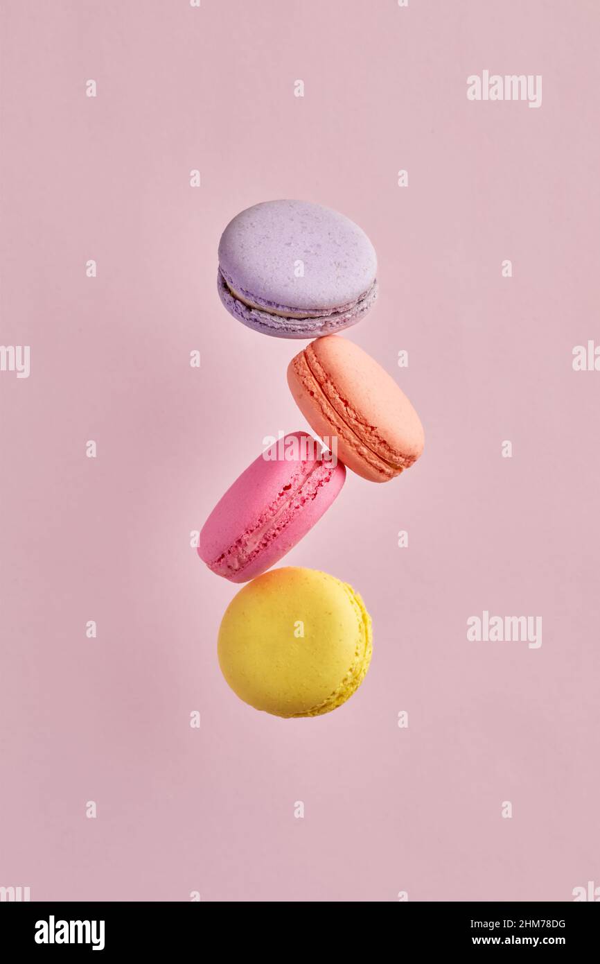 Délicieux dessert français coloré macaron ou macarons volant ou tombant en mouvement sur fond rose. Banque D'Images