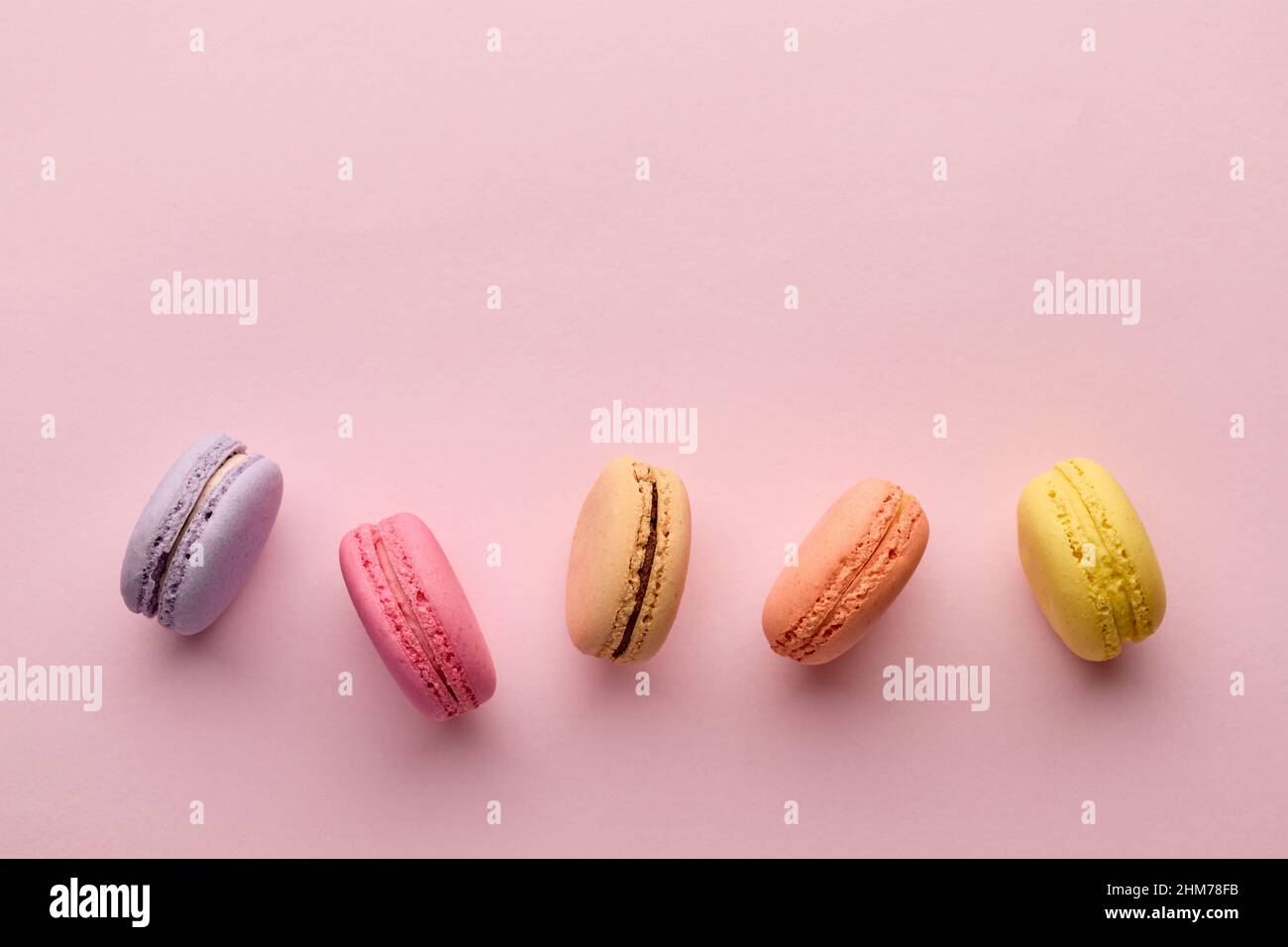 Délicieux dessert français coloré macaron ou macarons dans une rangée sur fond rose. Vue de dessus avec espace de copie. Banque D'Images