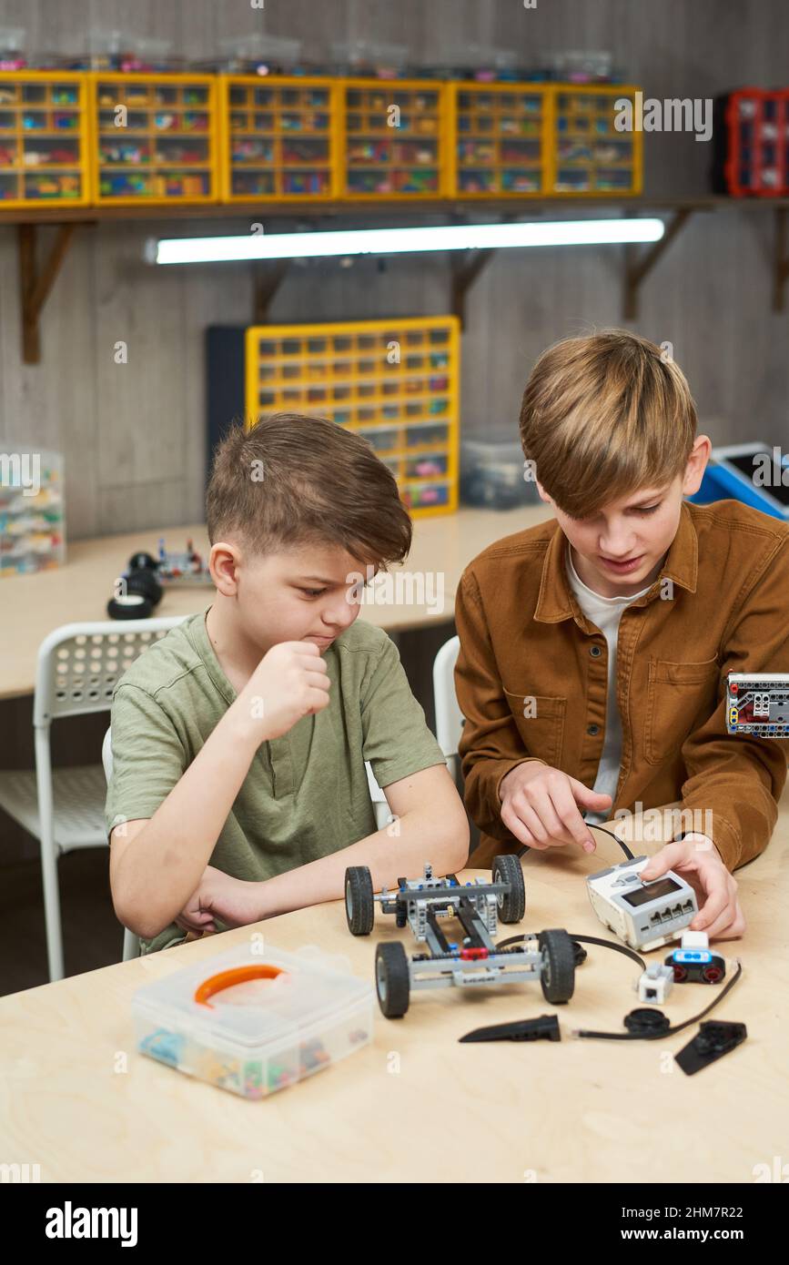 Portrait vertical de deux garçons assemblant la voiture électrique appréciant la classe de robotique à l'école Banque D'Images