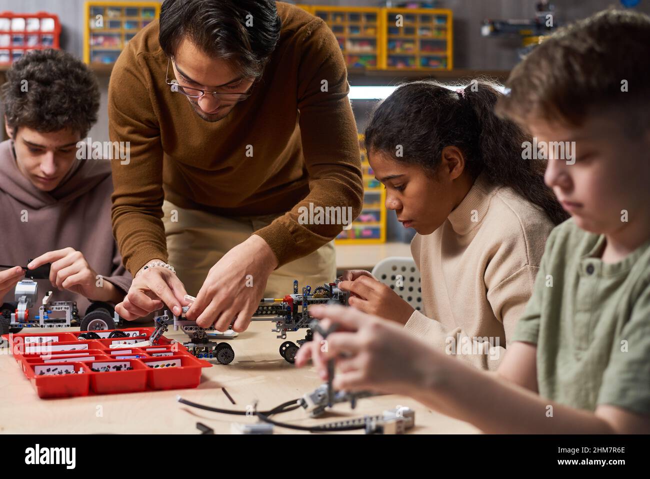 Portrait d'un jeune enseignant aidant divers groupes d'enfants à construire des robots dans la classe d'ingénierie à l'école moderne, l'espace de copie Banque D'Images