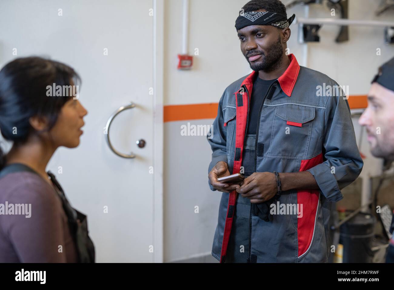 Portrait à la taille du jeune mécanicien afro-américain qui parle à ses collègues tout en travaillant dans un atelier de réparation automobile Banque D'Images