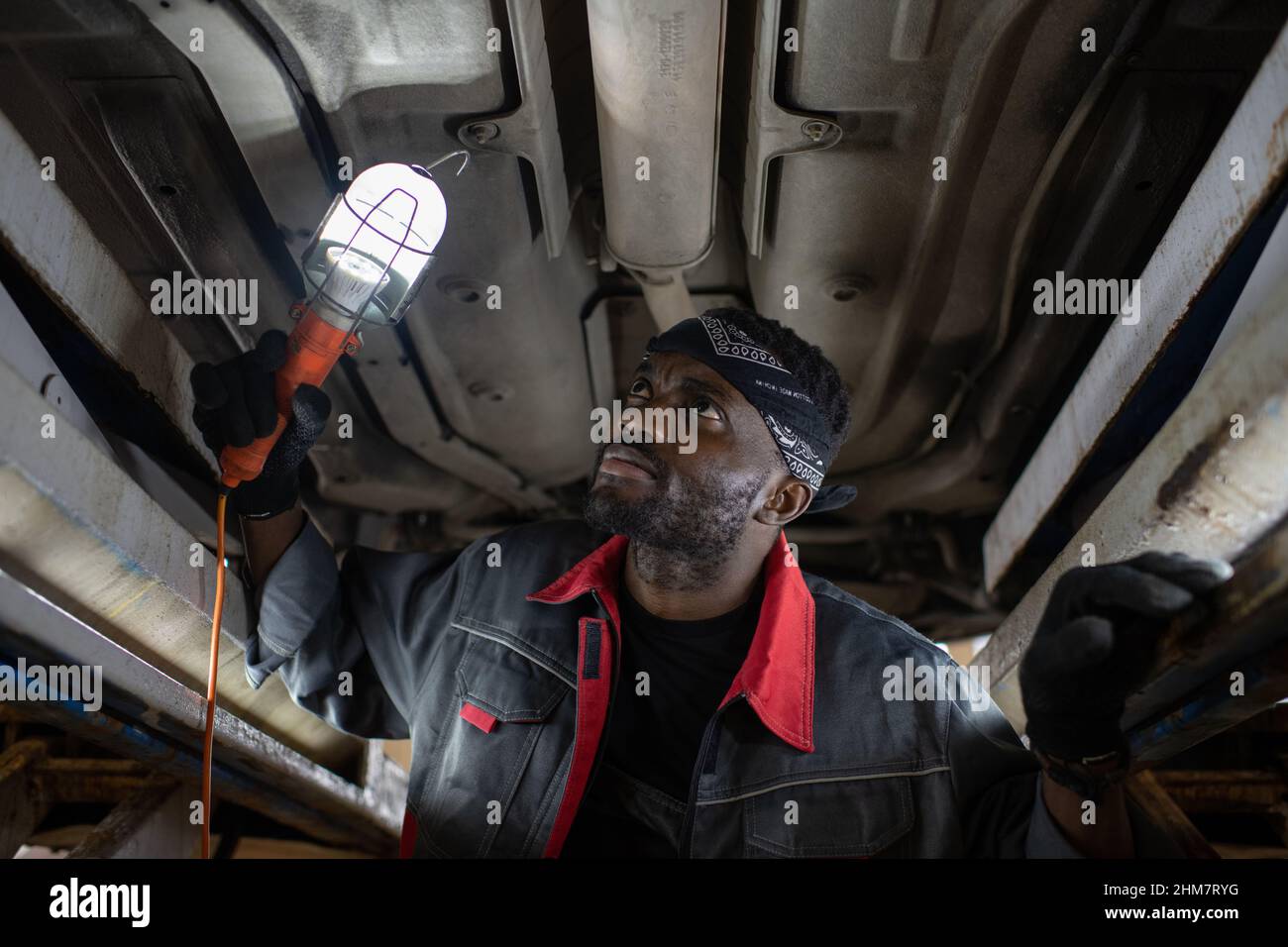 Portrait d'un mécanicien noir barbu inspectant la voiture sur un ascenseur dans un atelier de réparation automobile, espace de copie Banque D'Images