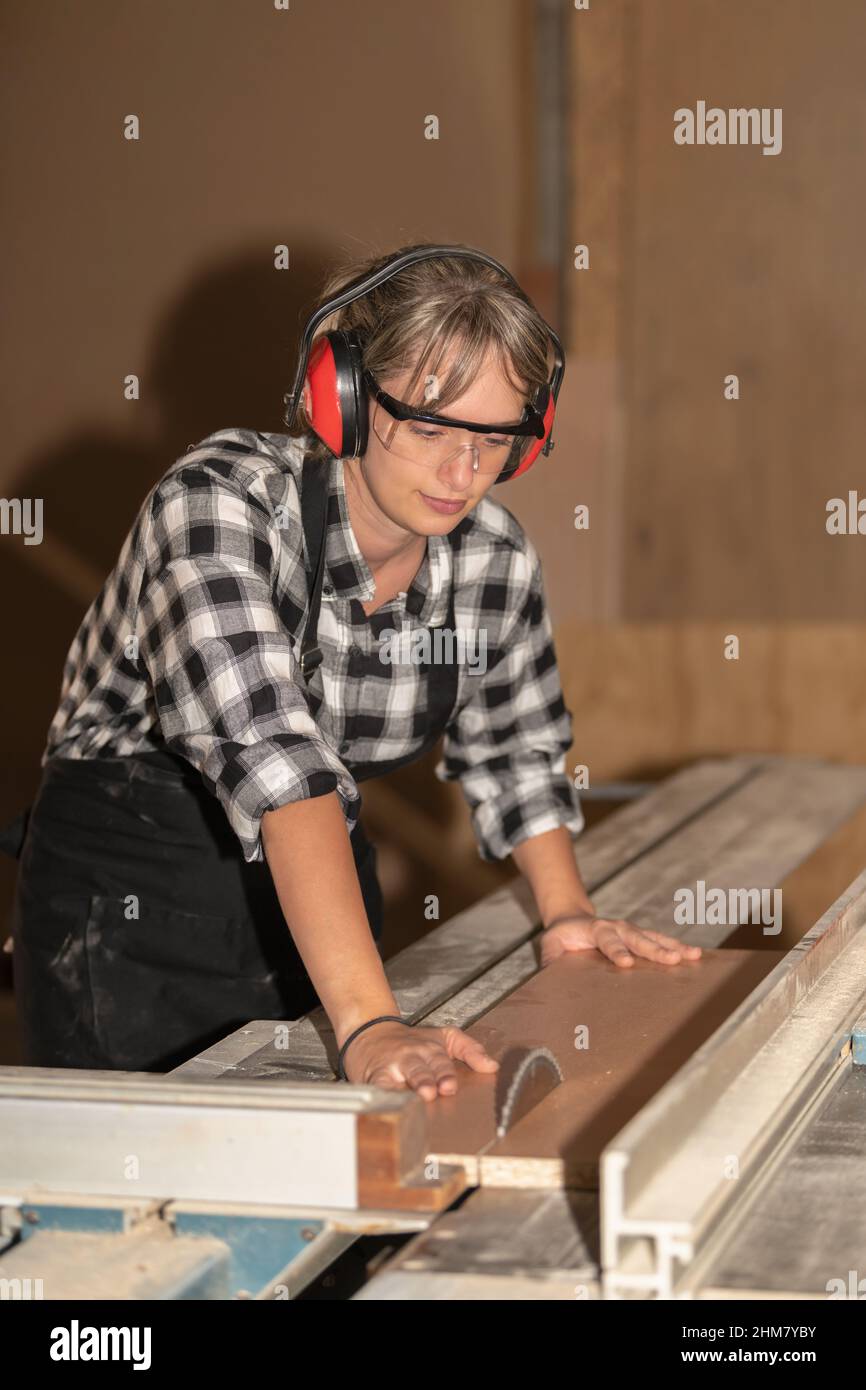 Femme concentrée coupant du bois dans un atelier de menuiserie Banque D'Images