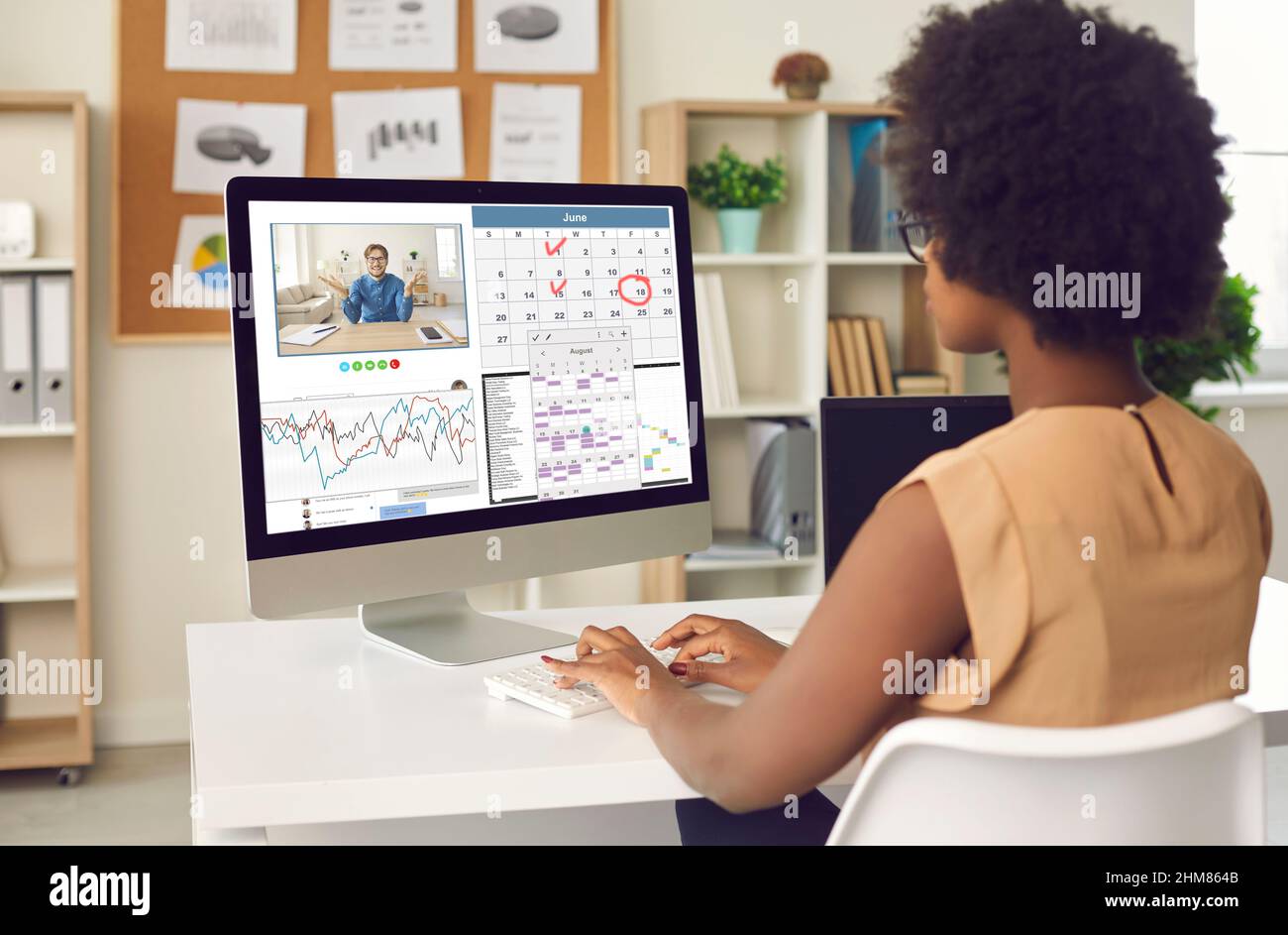 Femme noire travaillant sur un ordinateur de bureau, utilisant l'application de calendrier et ayant un appel vidéo Banque D'Images