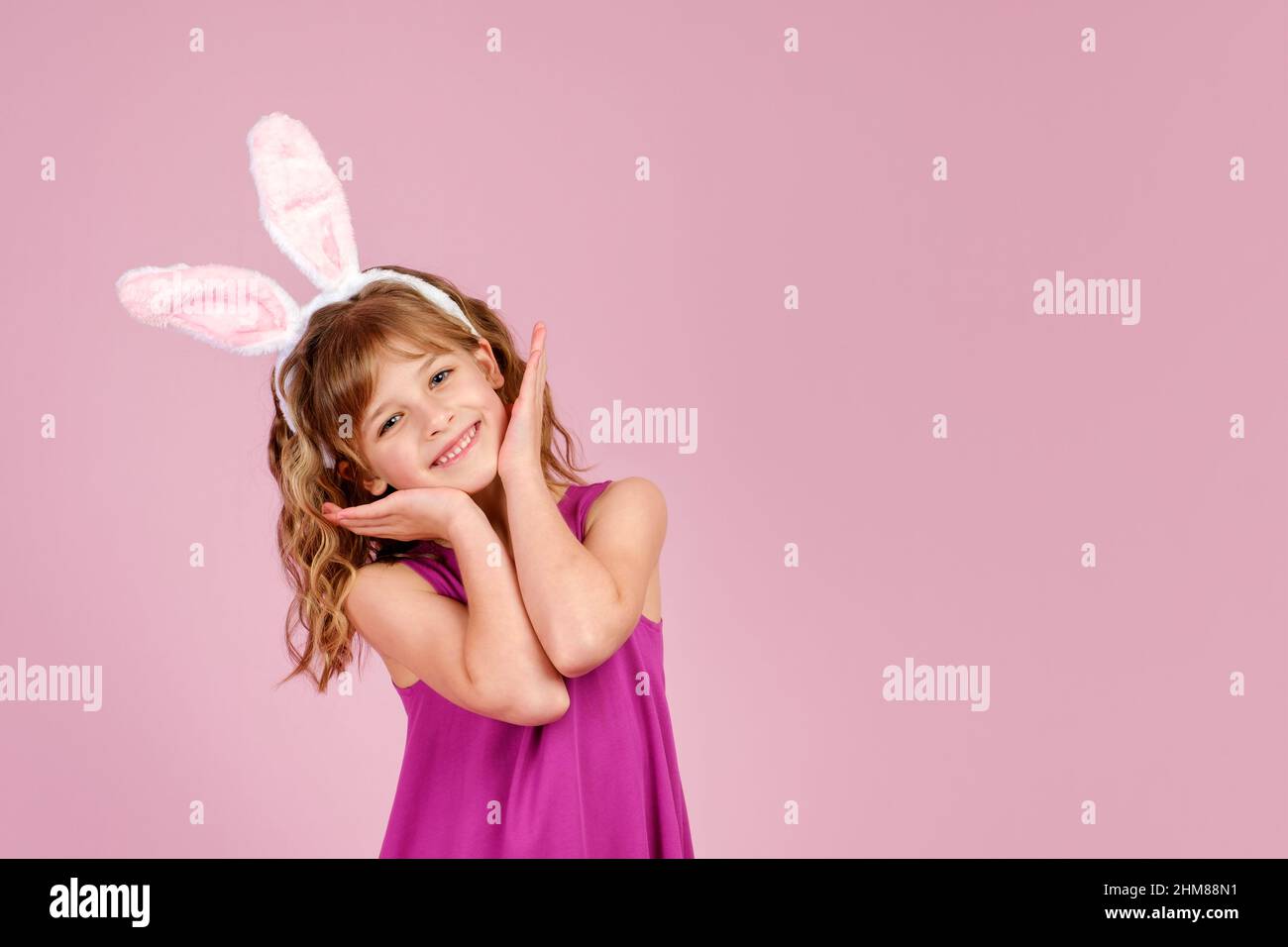 Adorable petite fille avec des oreilles de lapin touchant le visage et souriant en studio Banque D'Images