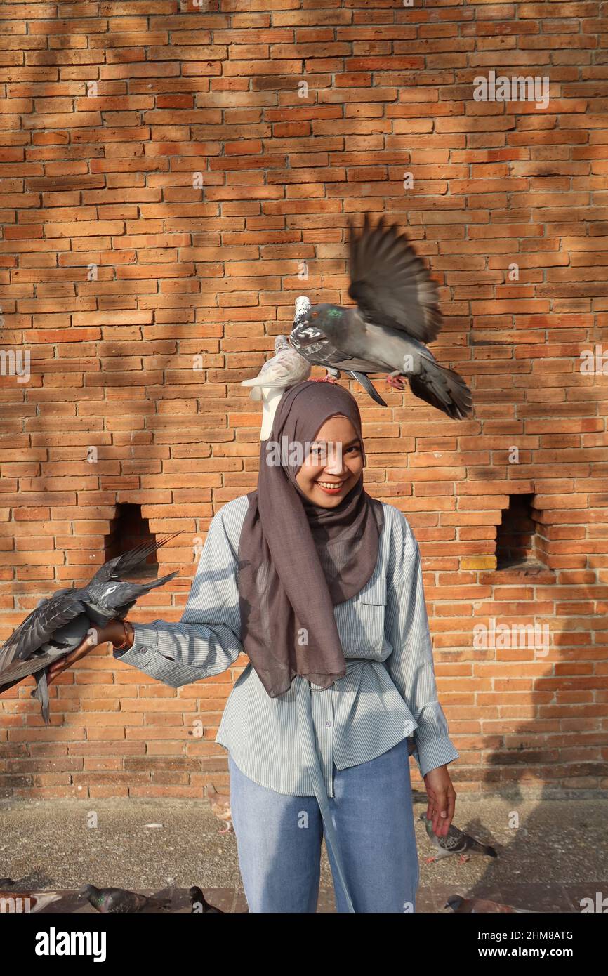 Femme thaïlandaise musulmane souriante avec des pigeons volant devant la porte de Tha Phae, Chiang Mai, Thaïlande Banque D'Images
