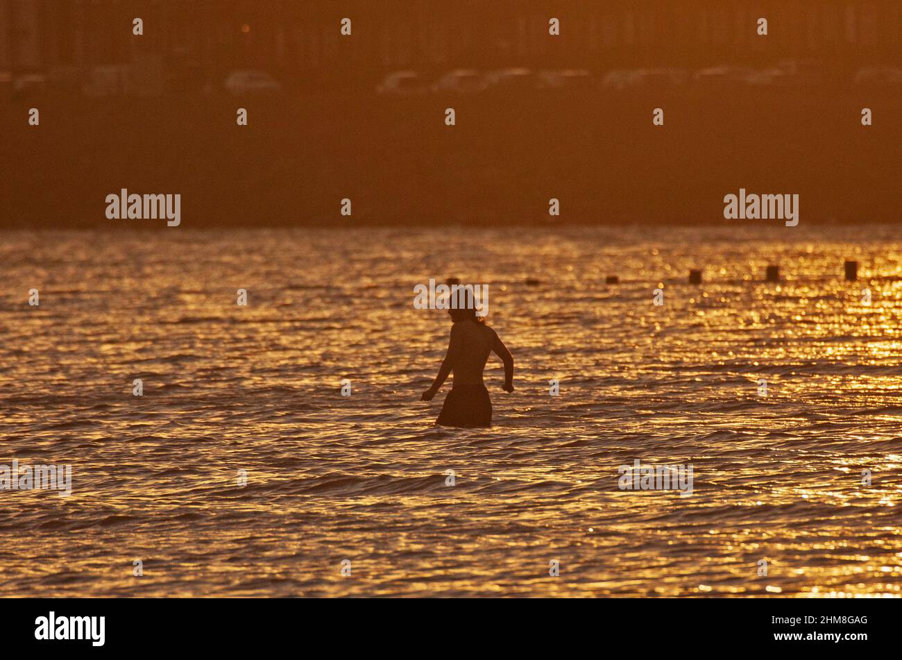 Portobello, Édimbourg, Écosse, Royaume-Uni. 8th février 2022. Rafraîchissez-vous au bord de la mer pour ceux qui font de l'exercice près du Firth of Forth. Température de 6 degrés centigrade. Contre-jour du lever du soleil, prise de vue contre la lumière provoquant des reflets du soleil dans le barillet de l'objectif, créant une image floue avec une lumière de bord autour des sujets, ce qui est un souvenir des anciennes images teintées sépia. Photo : un homme nageur d'eau froide fait son chemin de façon ggereuse dans l'eau froide. Banque D'Images