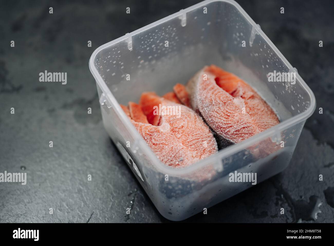 Vue de dessus du saumon rouge frais congelé. Steaks de saumon congelés dans une boîte ou un contenant en plastique sur fond gris foncé. Banque D'Images