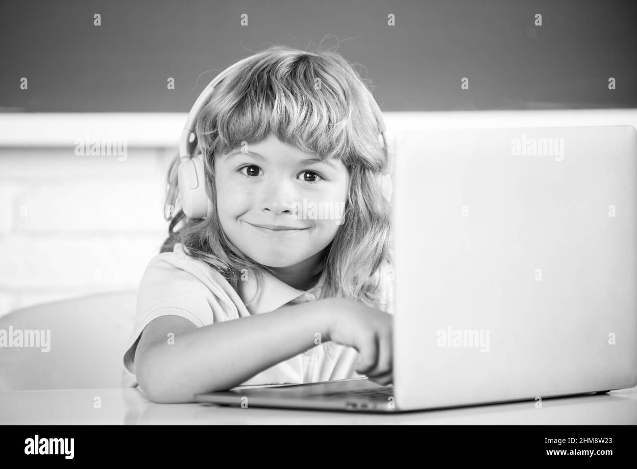 Smart drôle garçon dans le casque assis au bureau, étudier en ligne sur ordinateur portable à l'école, klever enfant porter des écouteurs dans l'apprentissage d'ordinateur portable en utilisant des leçons d'Internet Banque D'Images