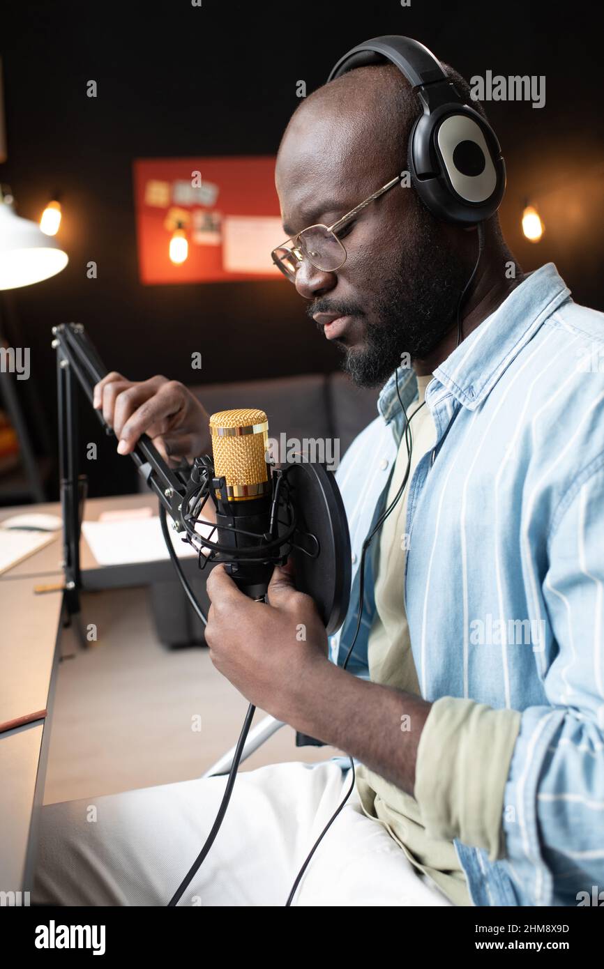 Un jeune homme africain dans un casque assis devant le microphone et se préparant à la diffusion en ligne Banque D'Images