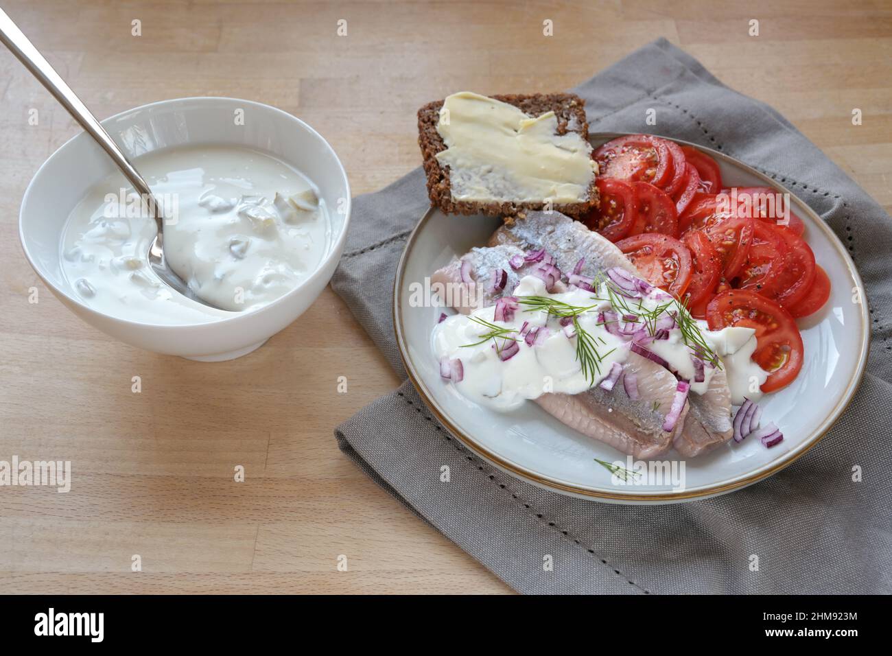 Filets de hareng salés avec tranches de tomate et pain complet brun sur une assiette et sauce à la crème aigre dans un bol, une serviette et une table en bois Banque D'Images